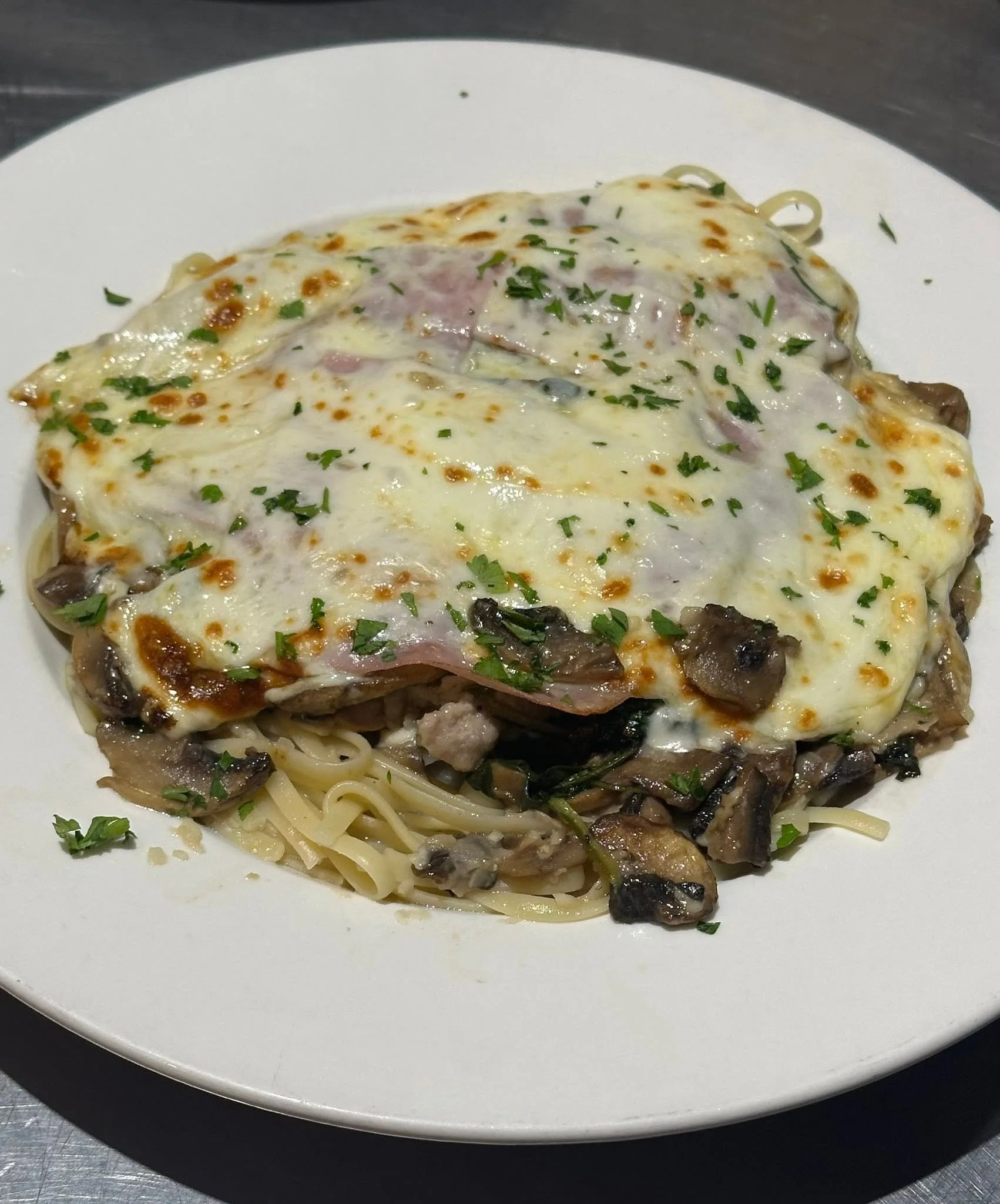 Plate of baked lasagna with melted cheese, parsley garnish, and visible layers of pasta, sauce, cheese, and meat.