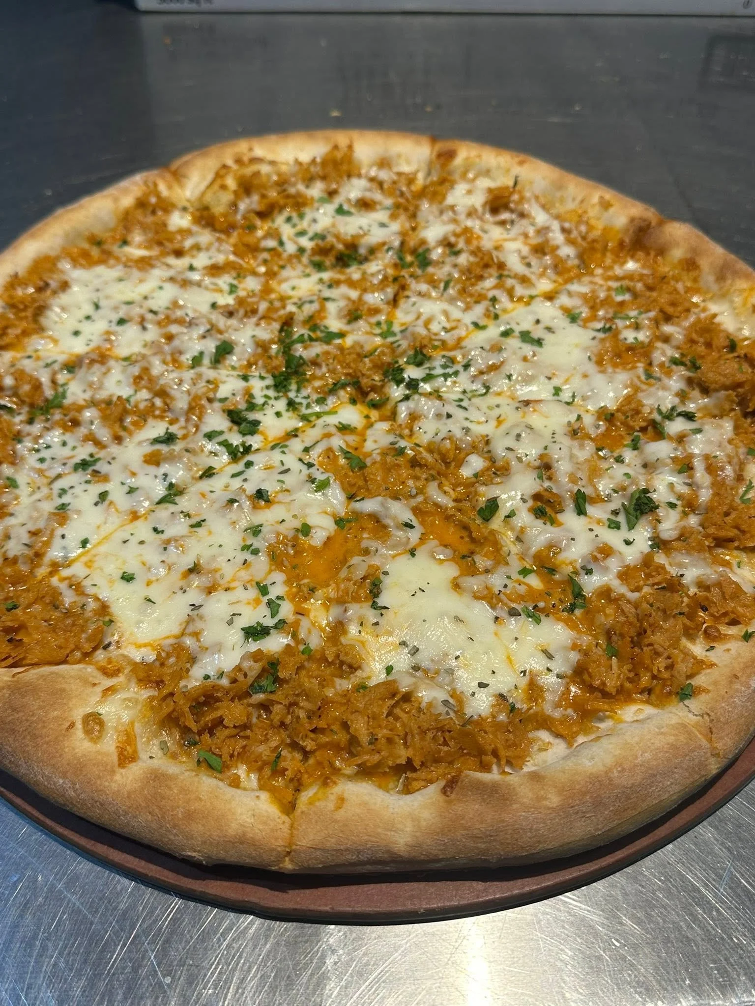 A pizza topped with shredded chicken, cheese, and sprinkled with chopped parsley.