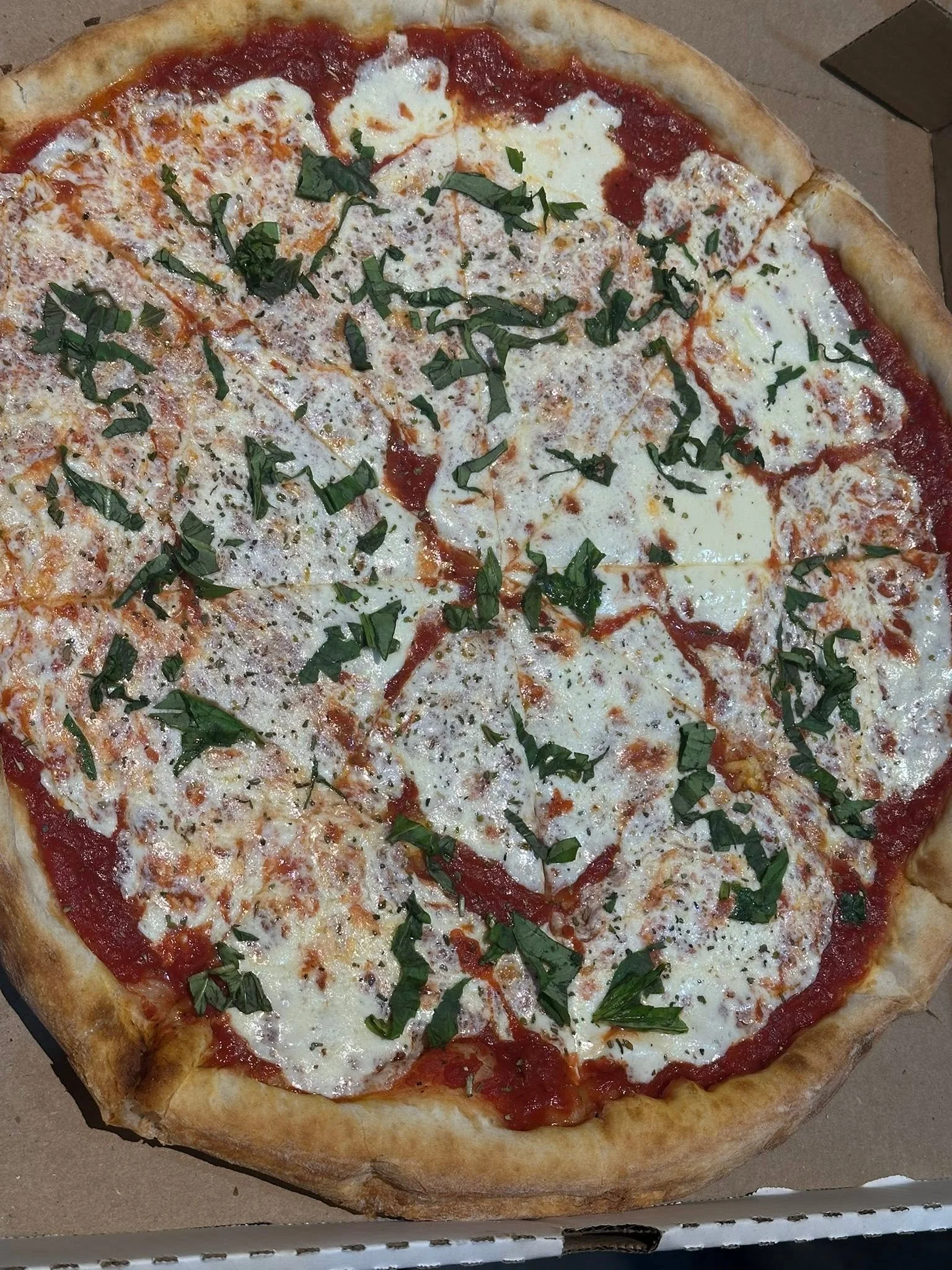 A large pizza topped with cheese, tomato sauce, and chopped fresh basil leaves.