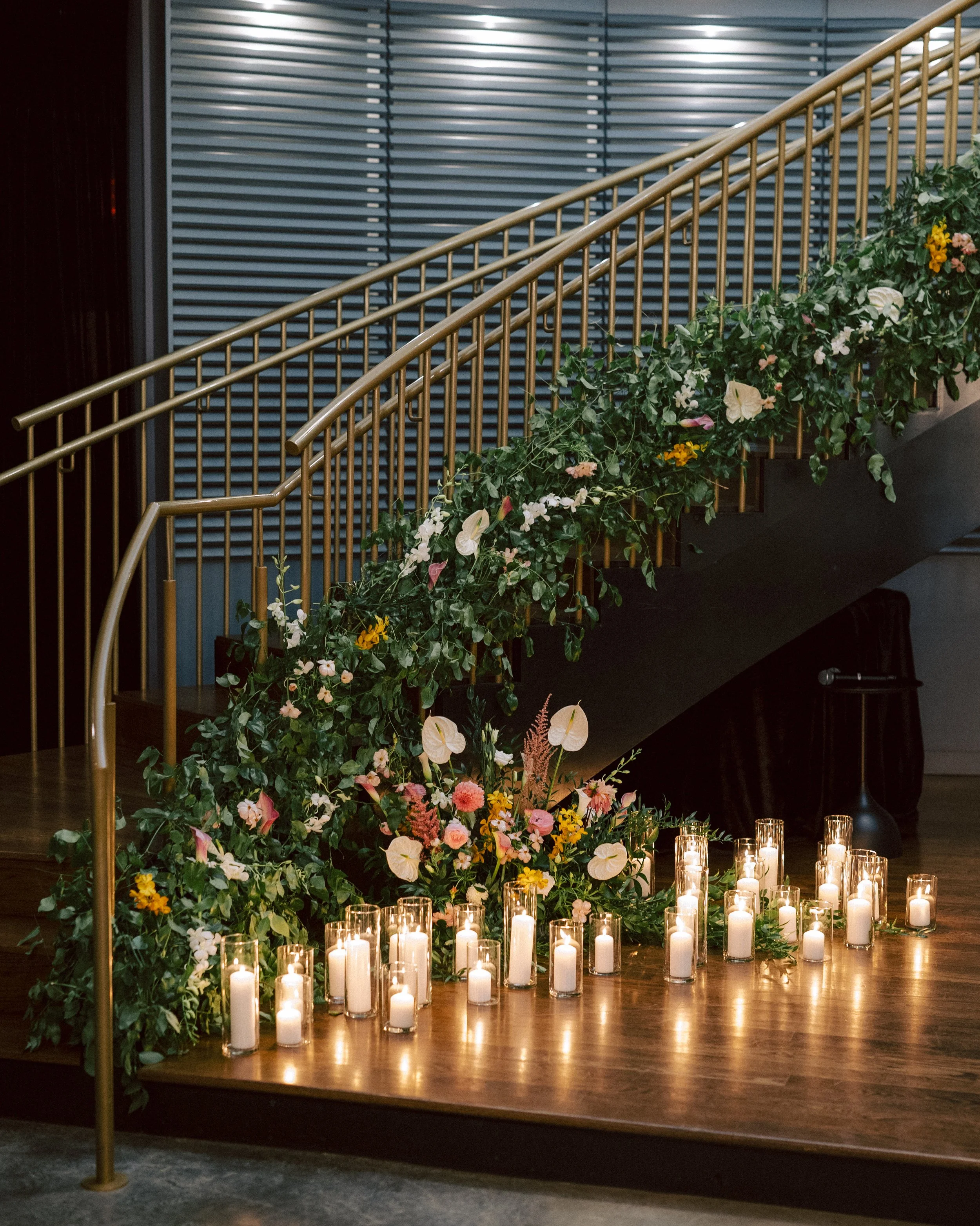 A staircase decorated with greenery and flowers, with candles in glass holders on the floor in front.