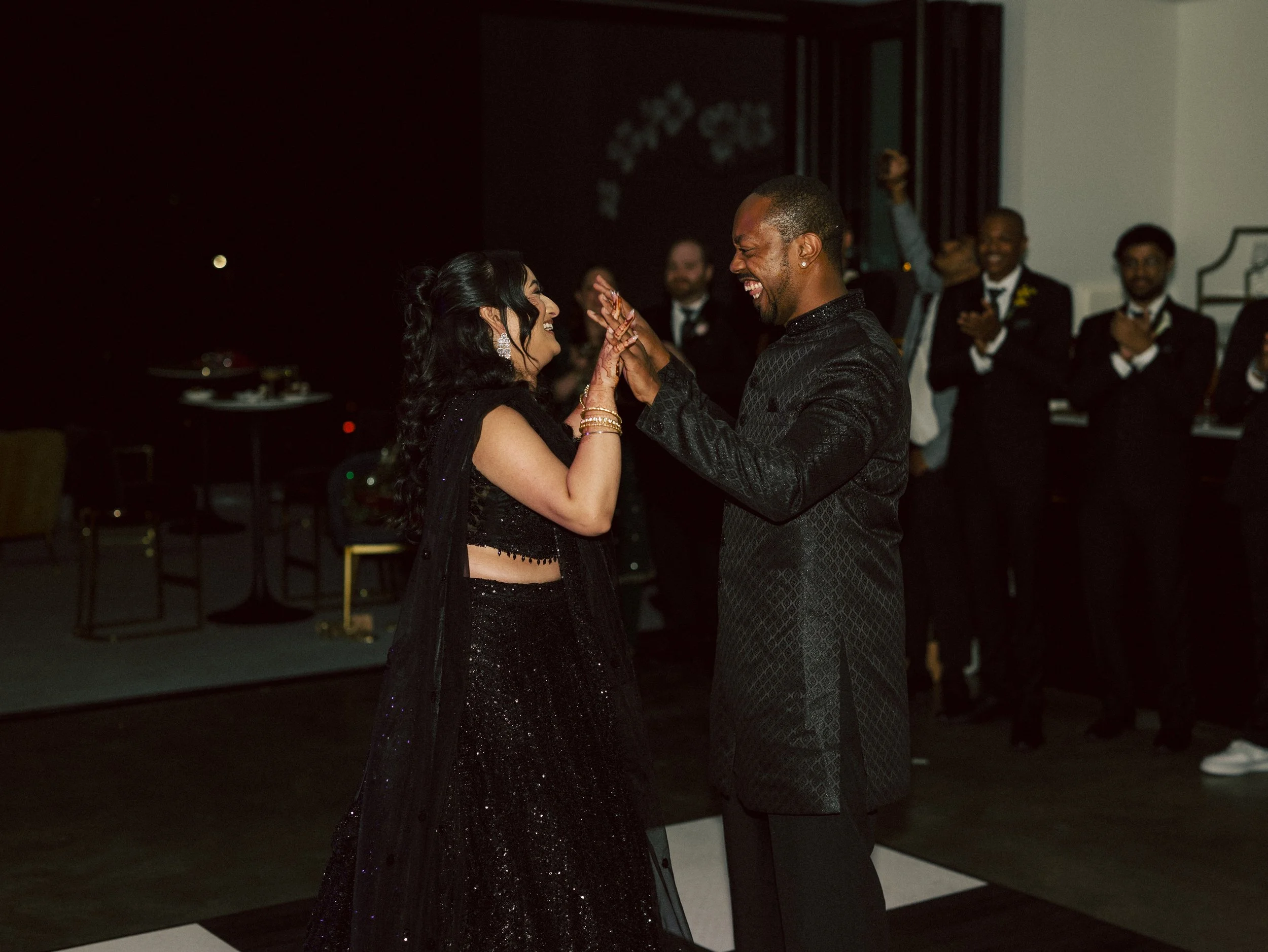 A couple dancing and smiling at a wedding reception, surrounded by applauding guests.