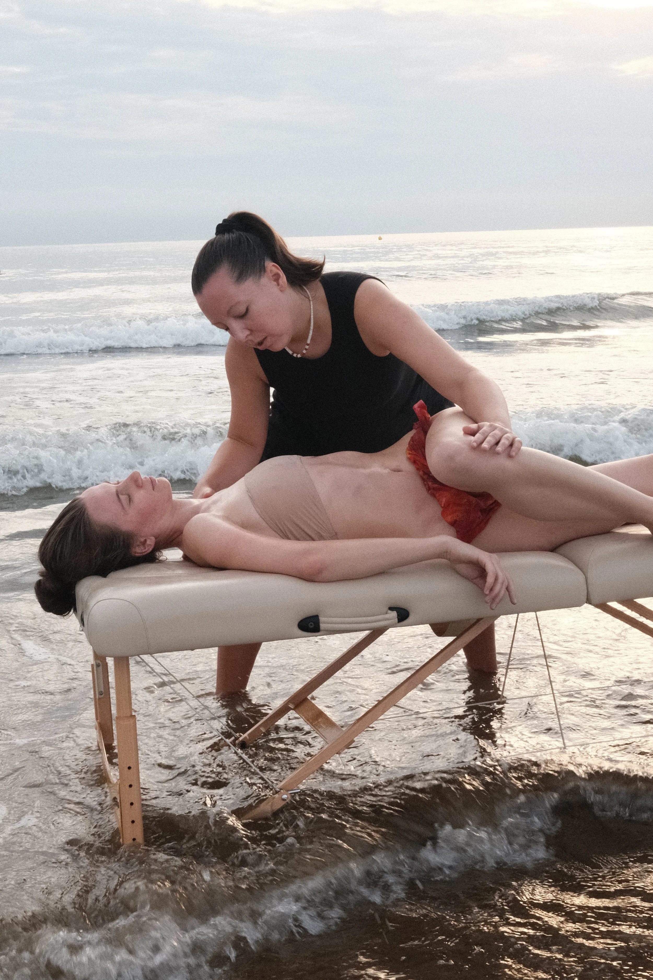 A woman receiving a Lomi Lomi massage on a massage table at the  Malvarossa beach with waves in the background.
