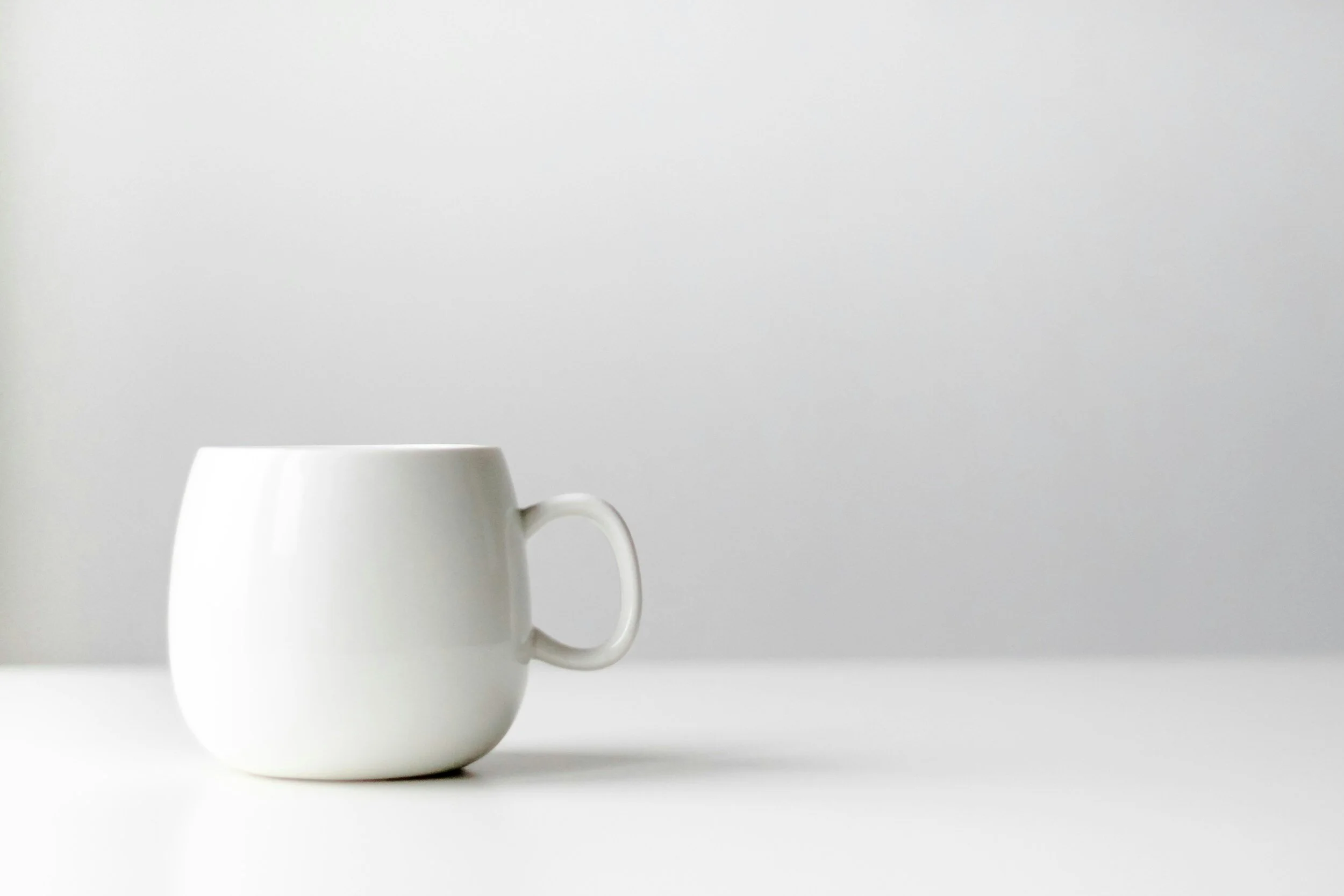 A white ceramic mug sitting on a white surface against a light gray background.