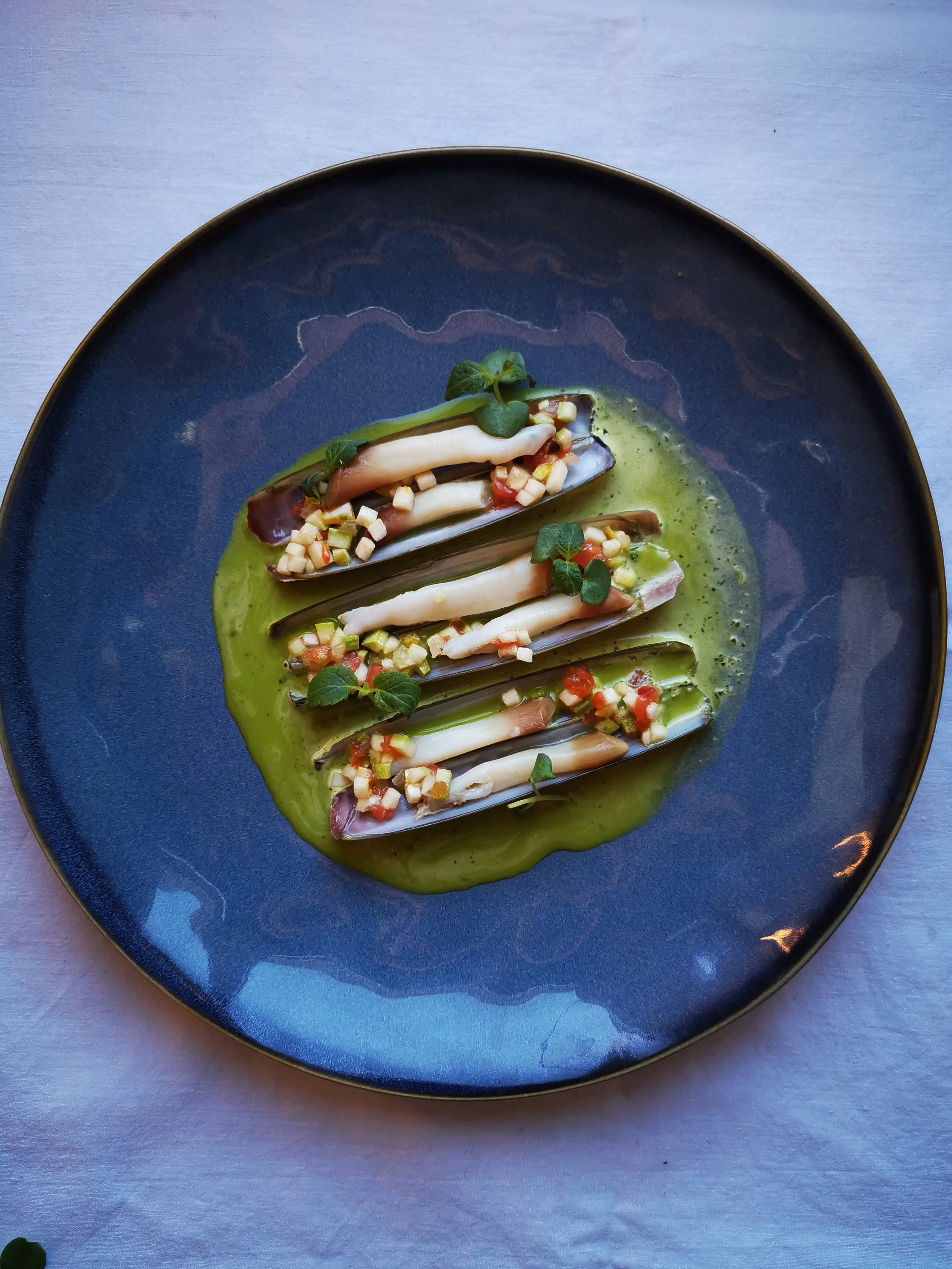 Assiette de fruits de mer sur un lit de sauce verte avec des légumes en dés et des herbes fraîches.