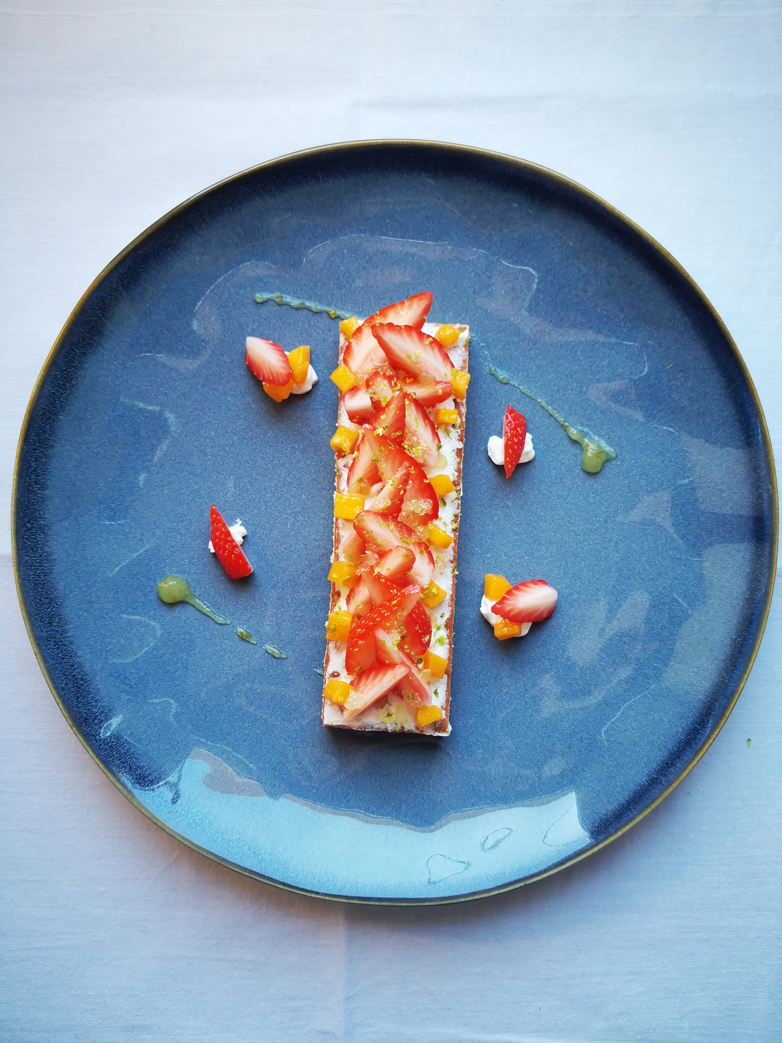 Dessert élégant avec des fraises et morceaux de mangue sur une assiette bleue.