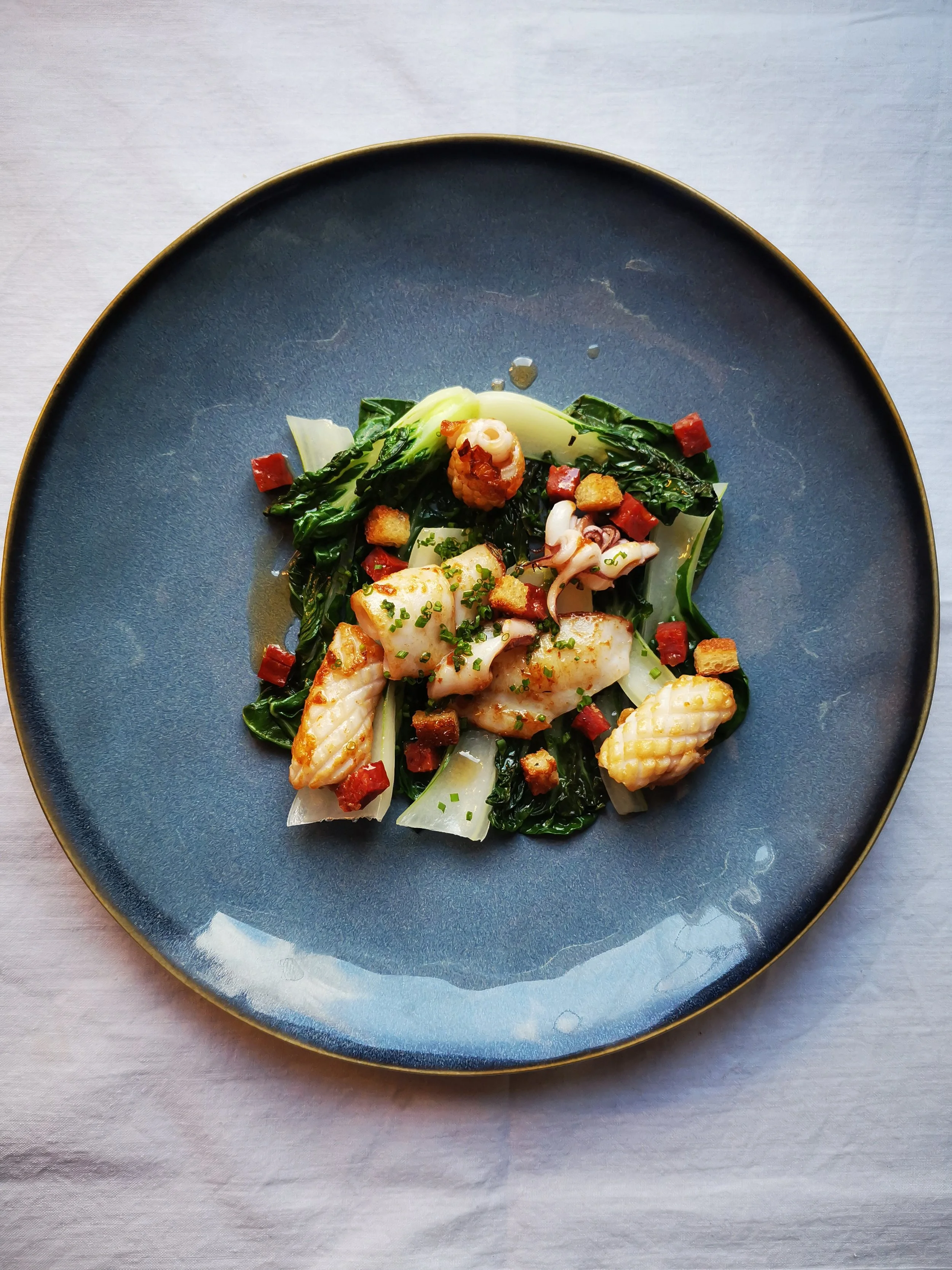 Assiette de calamar grillé avec des légumes verts et des croûtons, servie sur une assiette bleue.