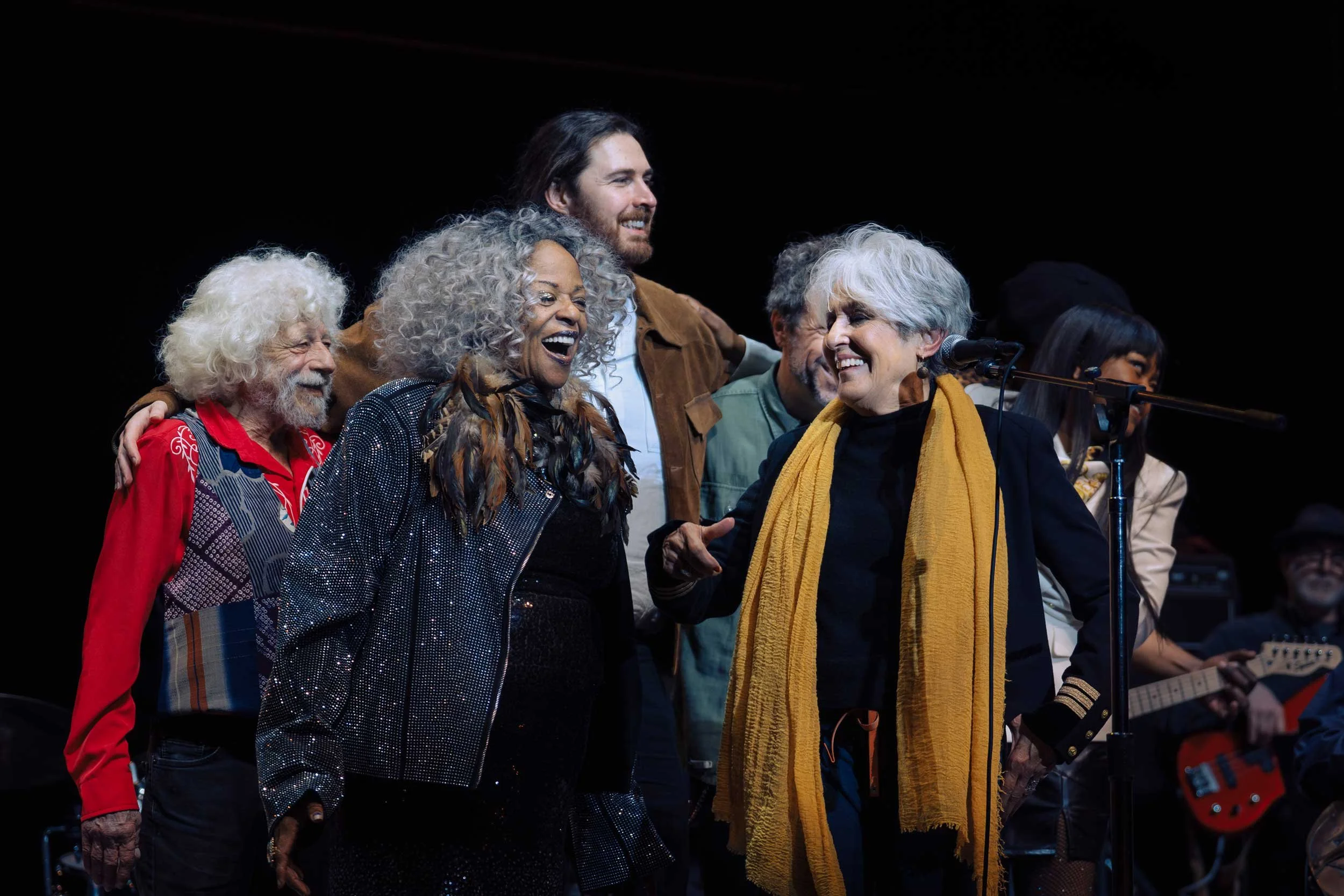 Group of diverse people on stage, smiling and enjoying each other's company during a musical performance.