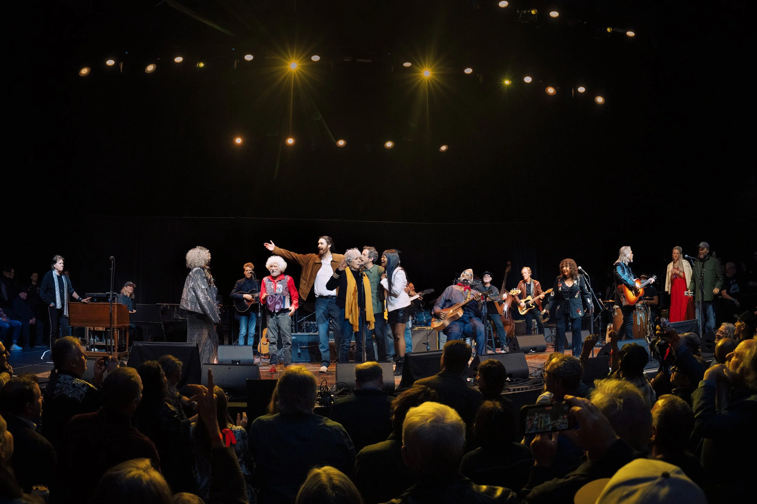 Musicians and performers on stage during a concert, with a large audience watching.