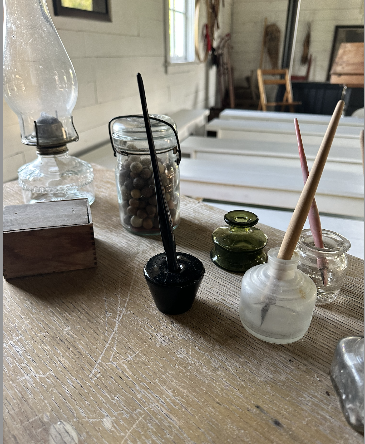 Collection of vintage glass jars and bottles with paintbrushes and pebbles on a wooden table in a rustic room.