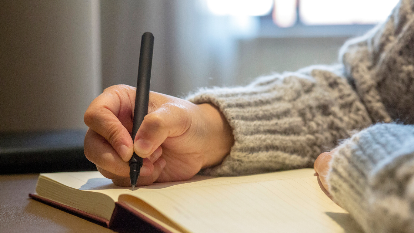 Hands of person in cozy sweater writing in a journal.