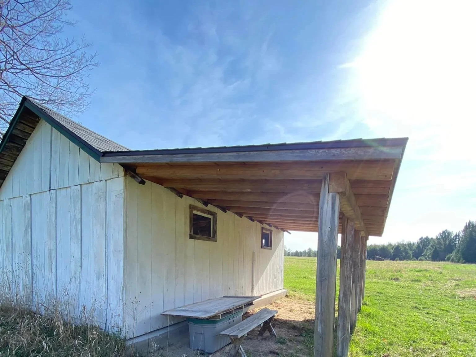 A rustic wooden barn with a slanted roof and small windows, located in a grassy field under a clear blue sky.