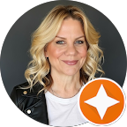 Woman with blonde hair smiling, wearing a black jacket and white shirt, with a grey background and an orange star badge in the corner.