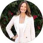 Woman with long brown hair smiling in front of flowering bushes