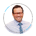 Close-up of a smiling man wearing glasses, a blue and white striped shirt, and a blue tie, with a white background.