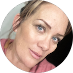 Close-up of a woman's face with light makeup and brown hair, looking at the camera.