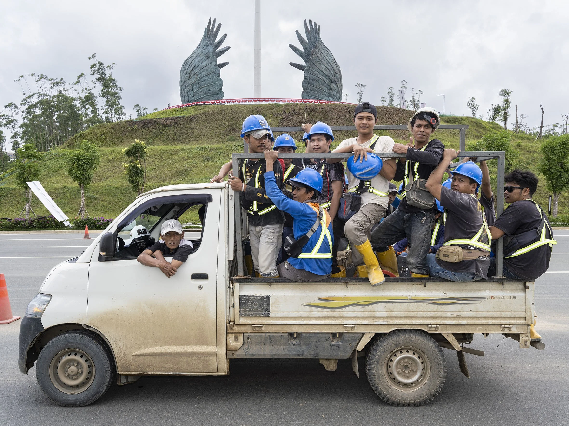 Construction workers in the back of a pick-up truck drive past the Nusantara Pritective Wings monument. 24 August 2025