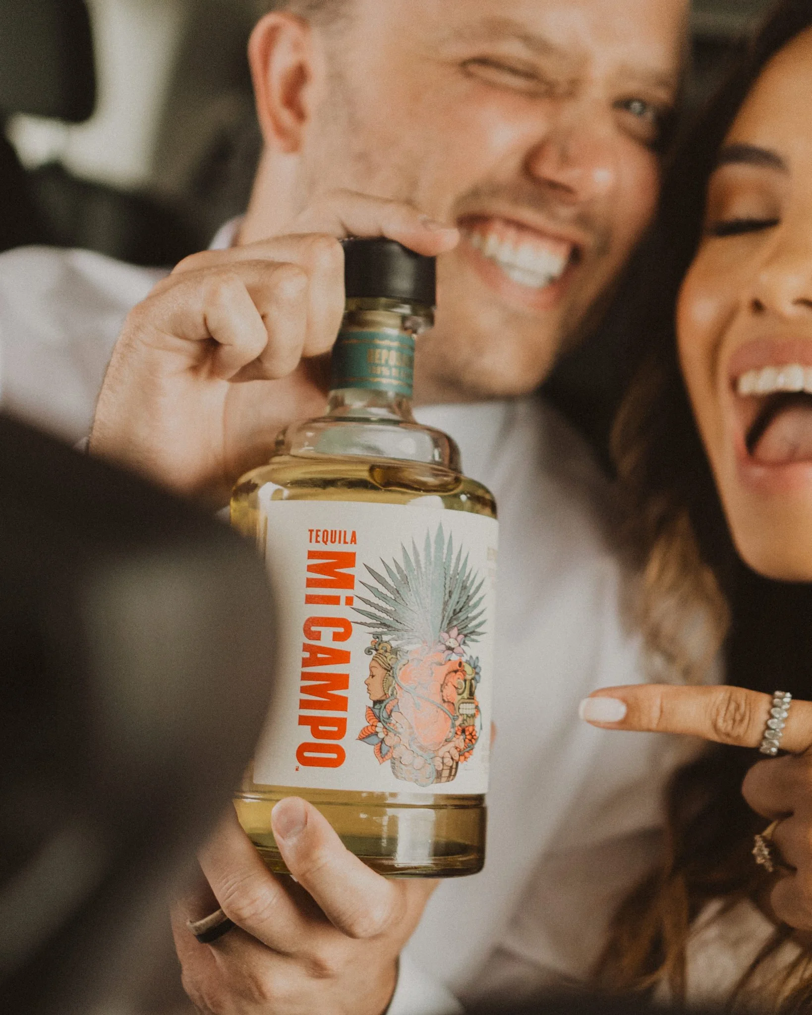 Newly eloped couple laughing together in the car while holding a bottle of tequila to celebrate their Alaska elopement