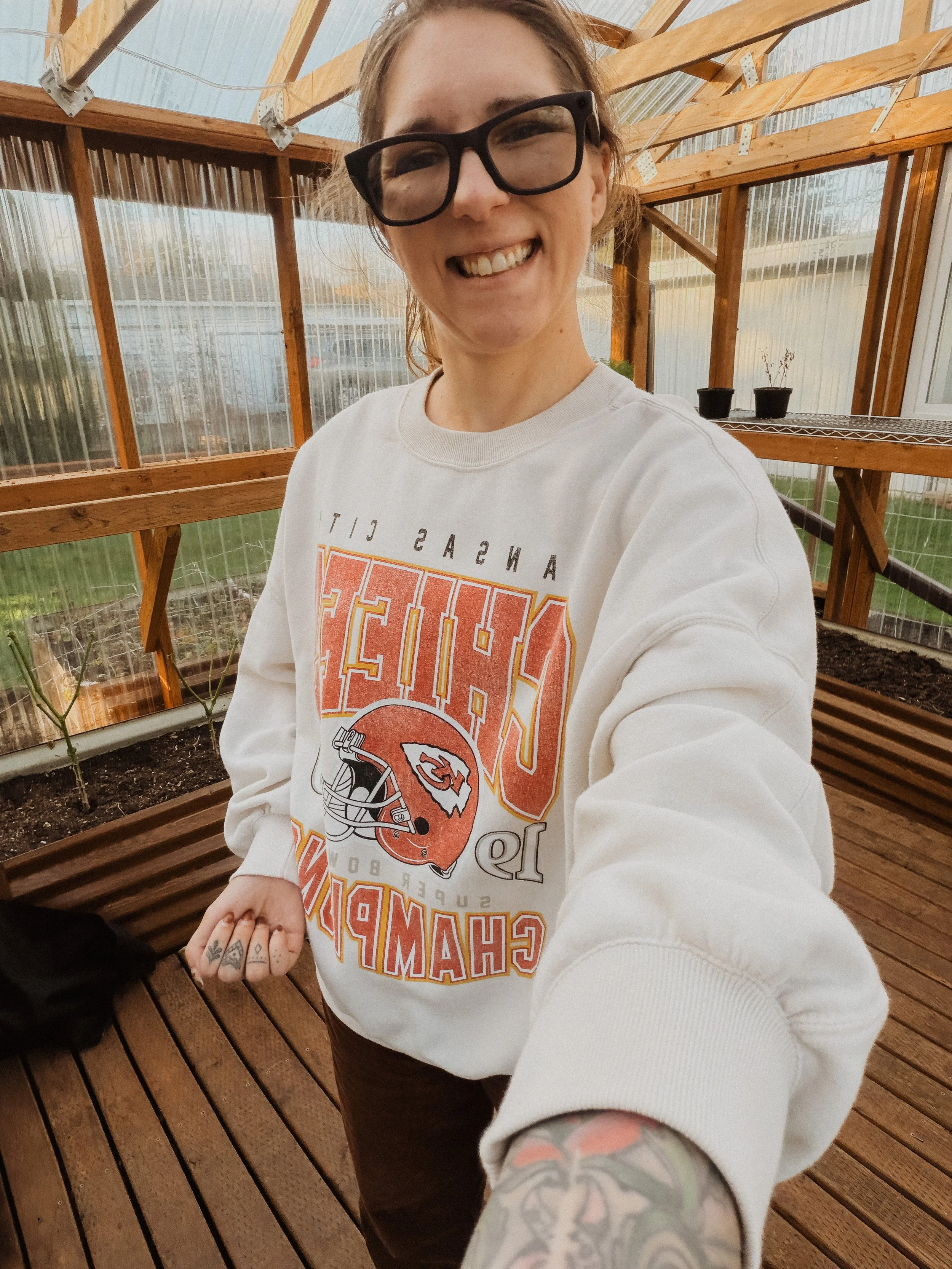 Paige Kleckner wearing tan and red Kansas City Chiefs NFL sweatshirt inside greenhouse