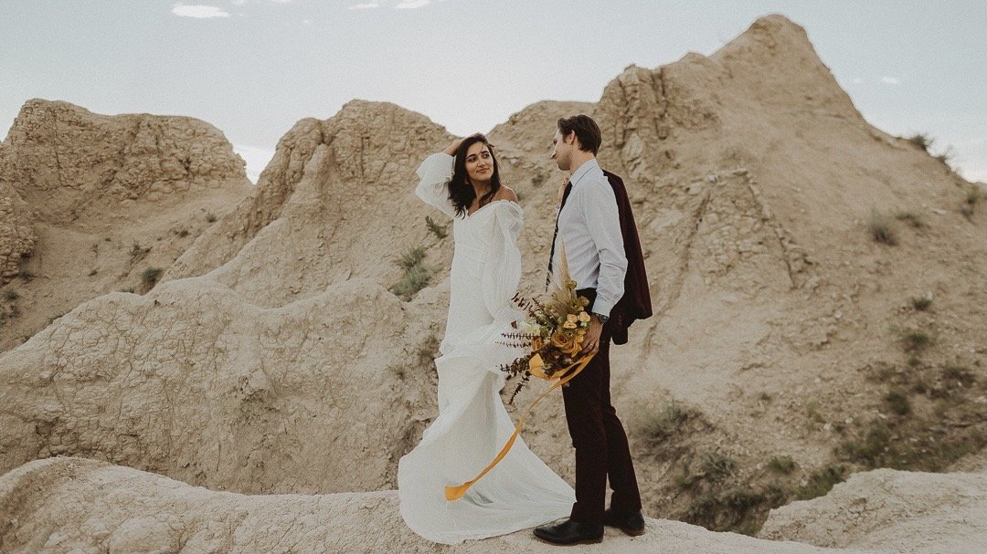 bride grinning at groom in maroon suit in Badlands National Park