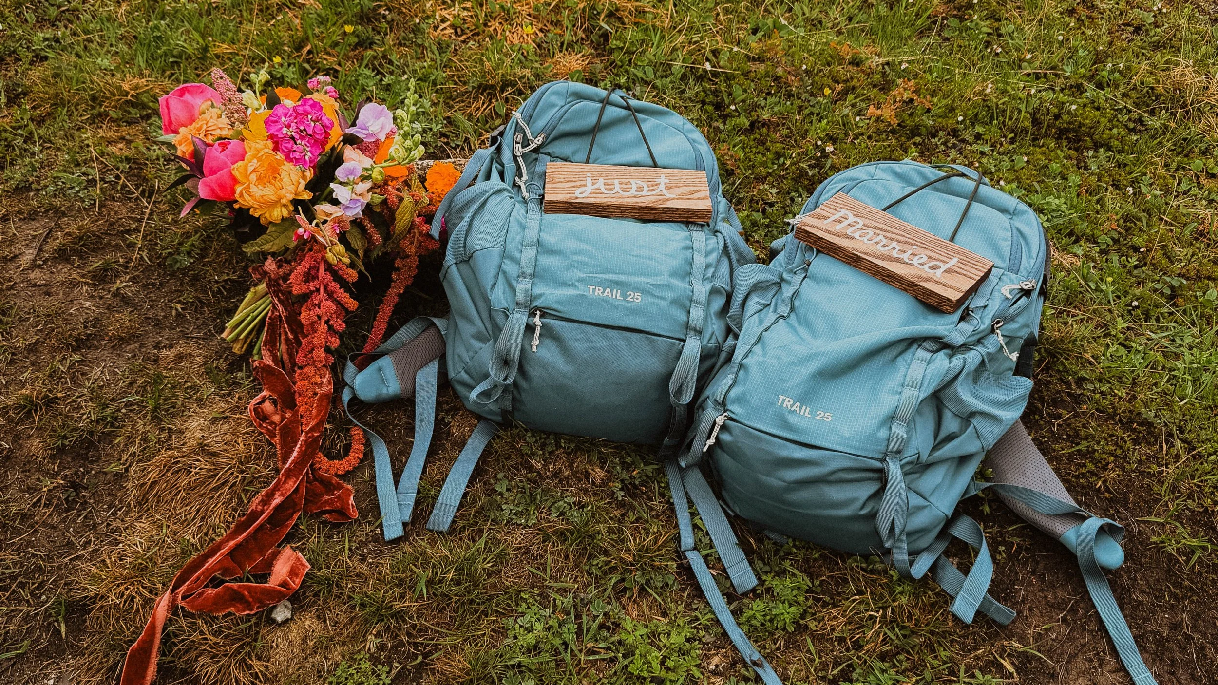 blue hiking backpacks with wooden just married signs next to irange and red bouquet of flowers