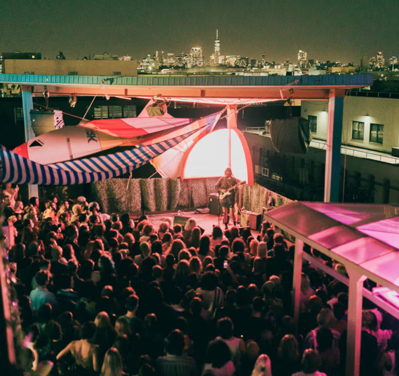 crowd watching a live performance on elsewhere's rooftop with the manhattan skyline behind