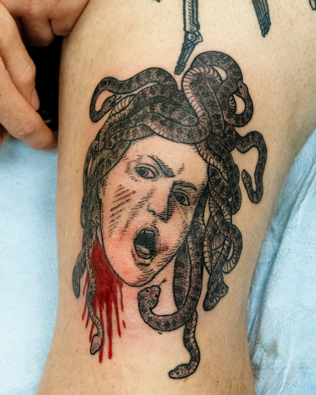 Tattoo of a woman's face with snakes for hair, resembling Medusa, with blood dripping from her neck.