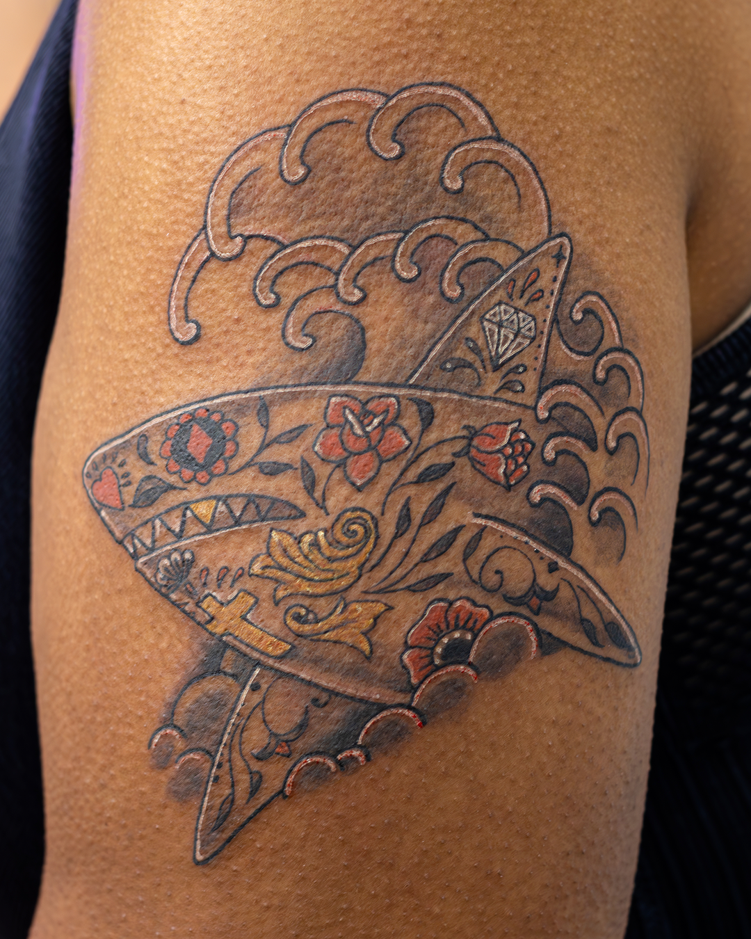 Tattoo of a shark with floral and decorative patterns on a person's upper arm.