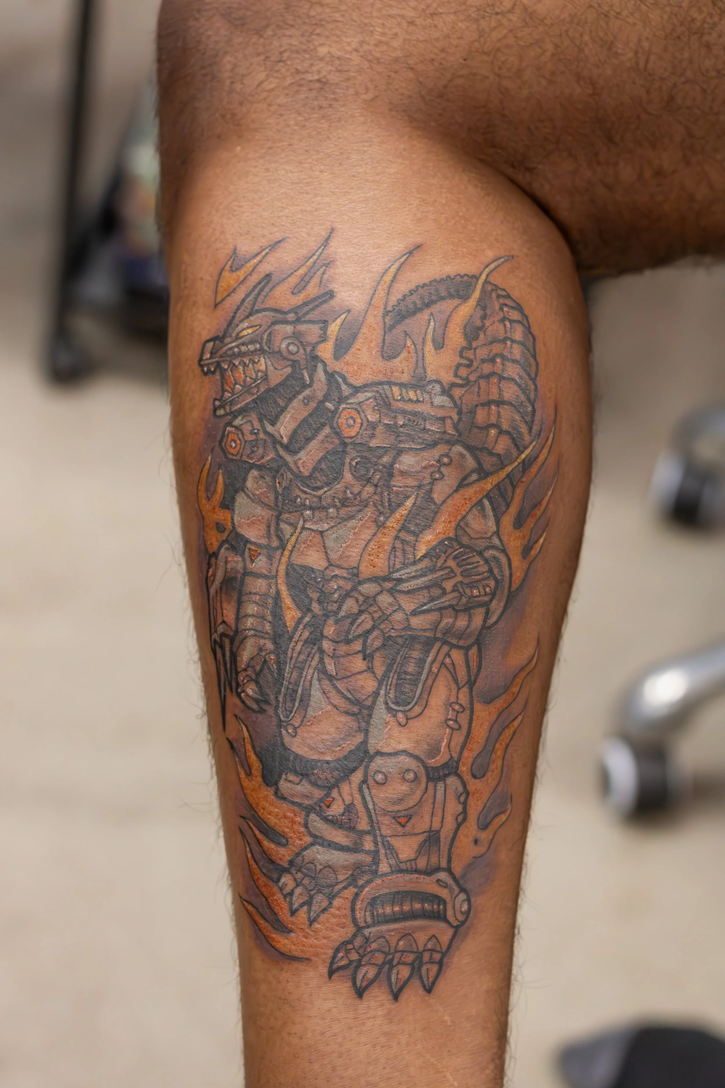 Tattoo of a robotic dragon on a person's thigh with flames and mechanical details.