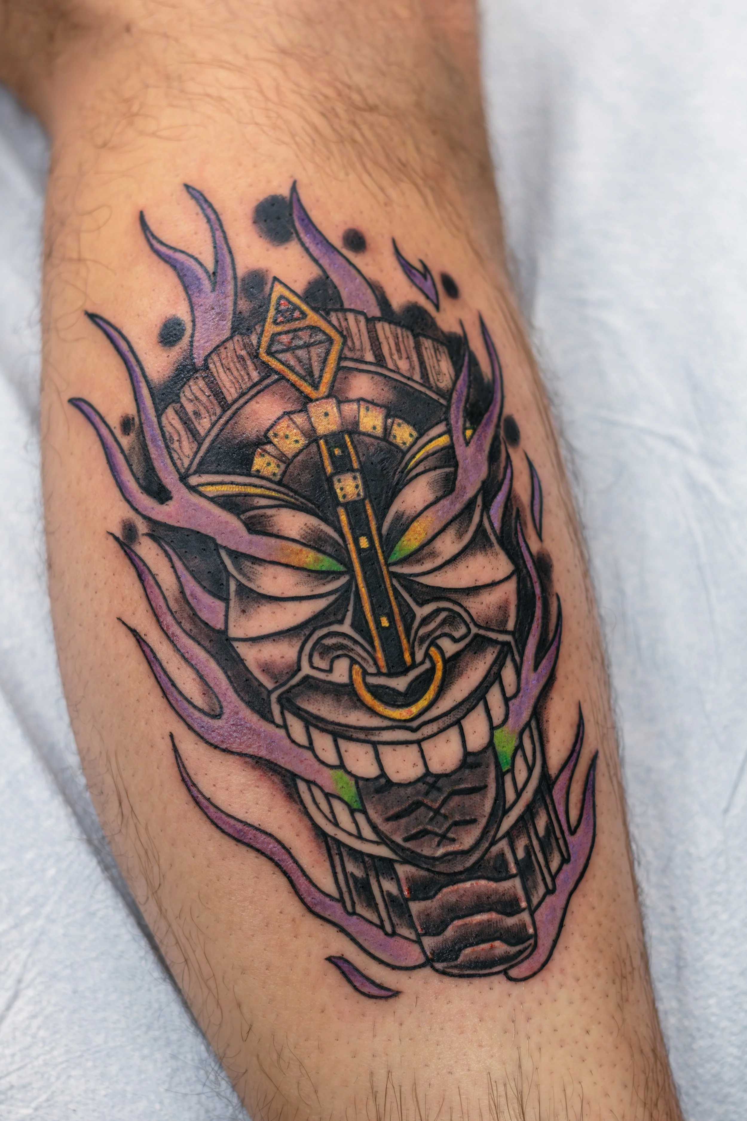 Colorful tattoo of a smiley face mask with purple flames surrounding it.