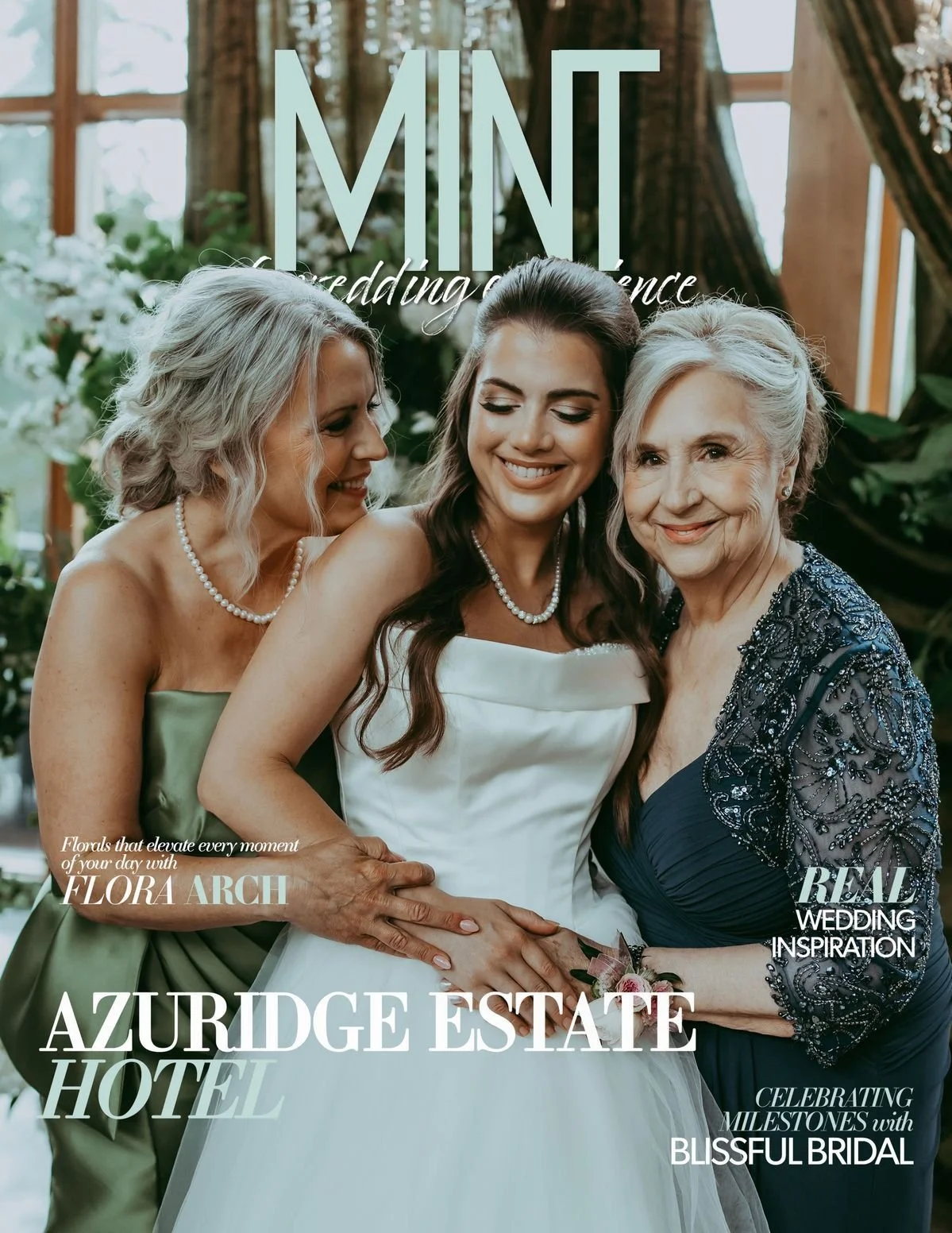 A bride in a wedding dress standing between two women, possibly her mother and grandmother, smiling at the camera, with floral decorations and windows in the background.
