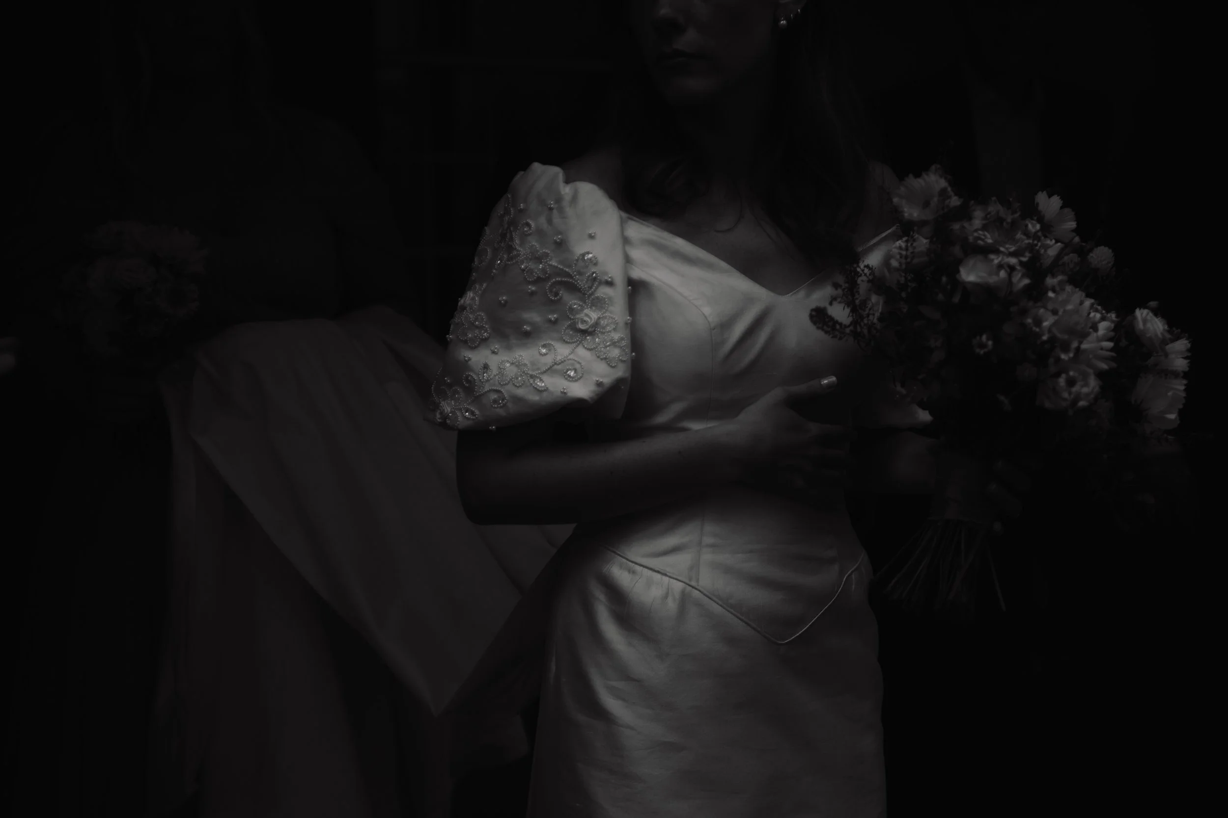 A bride in a wedding dress holding a bouquet of flowers, standing indoors.