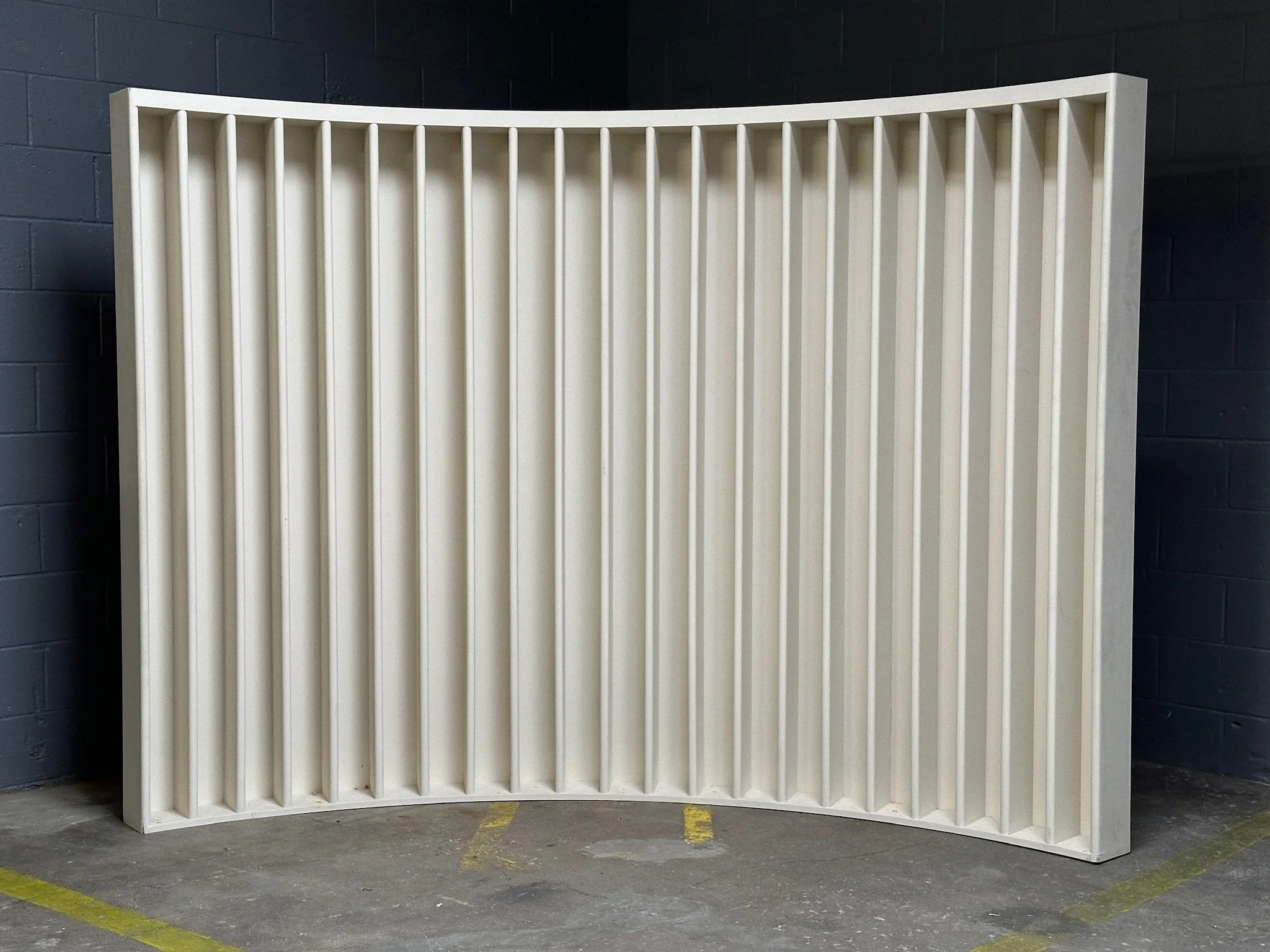 White curved room divider or backdrop with fluted vertical slat detail.
