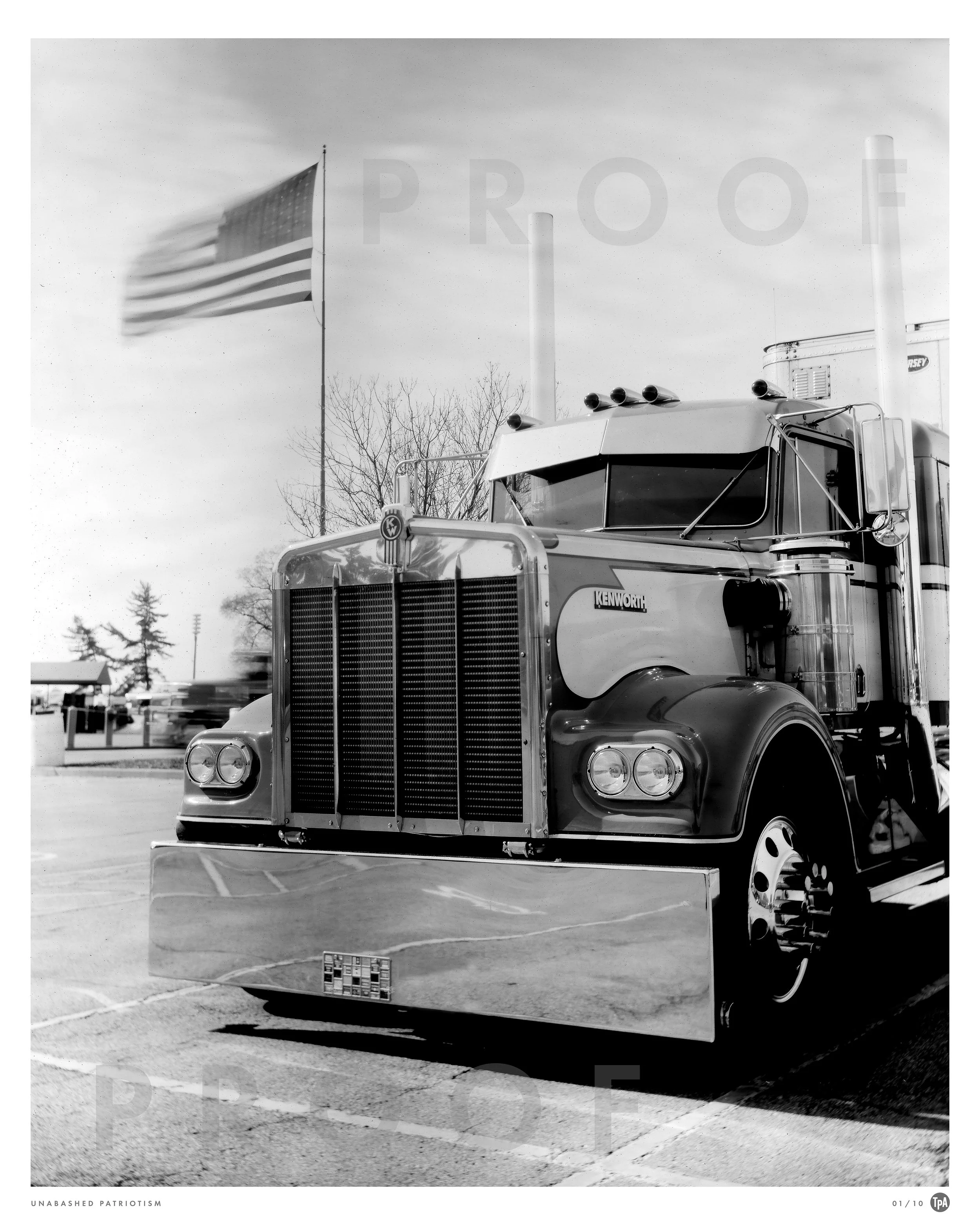 Black and white photo of a semi-truck with a Kenworth badge, parked in a lot. An American flag waving in the background. The sky is partly cloudy.