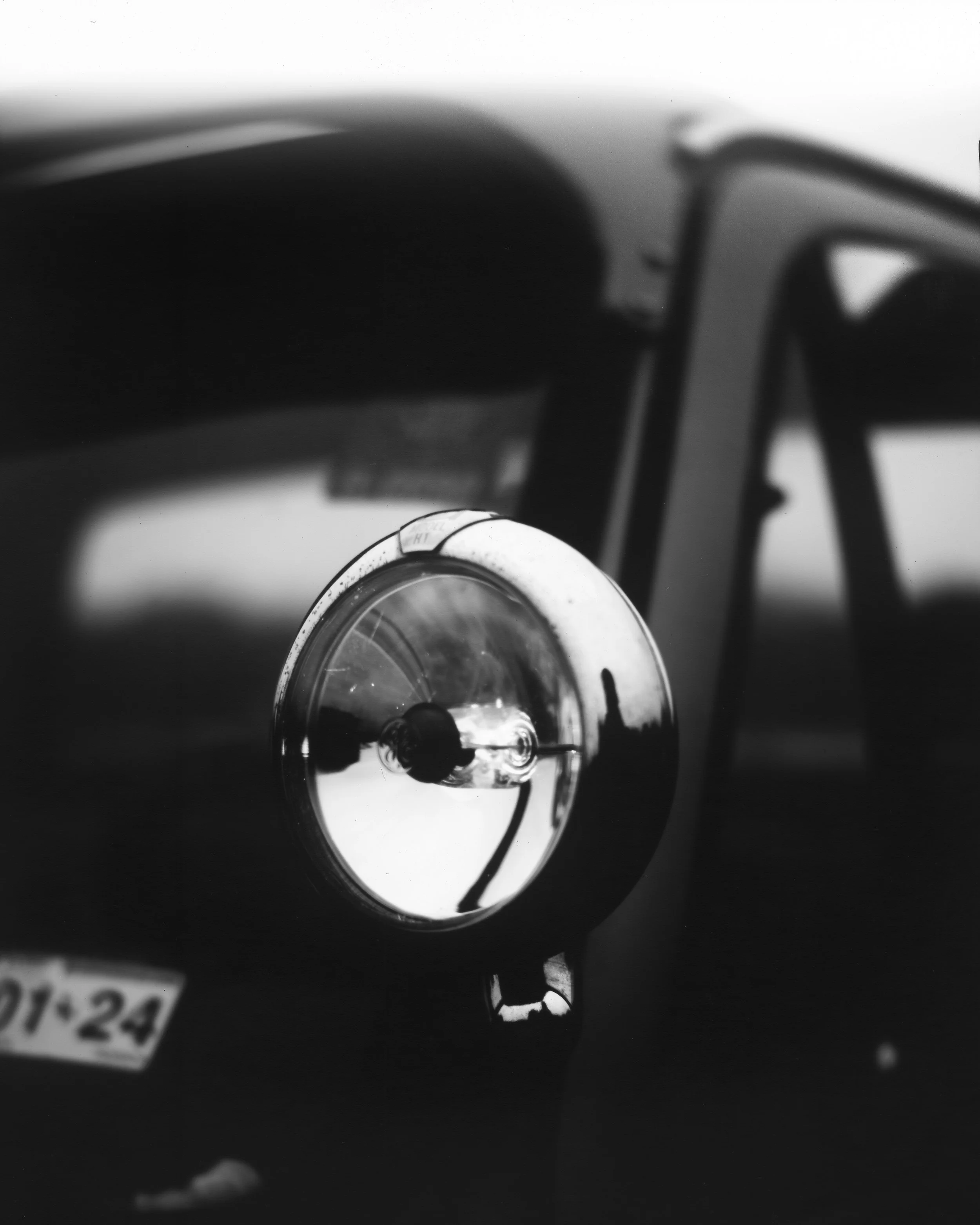 Close-up of a vintage car's headlight with a reflection of the sky and surrounding environment, in black and white.