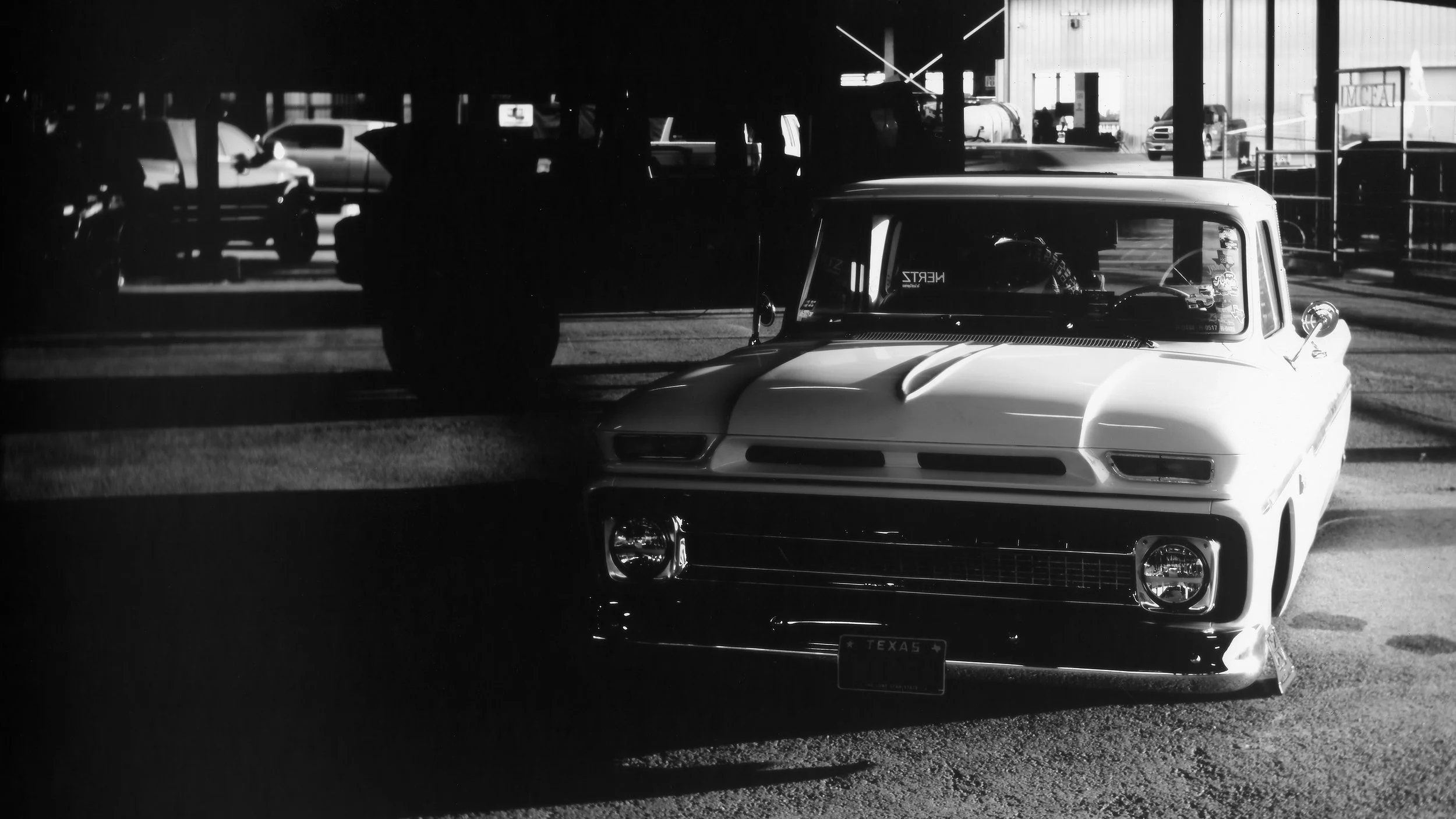 Black and white photo of a vintage car parked in front of a building with shadowy background.