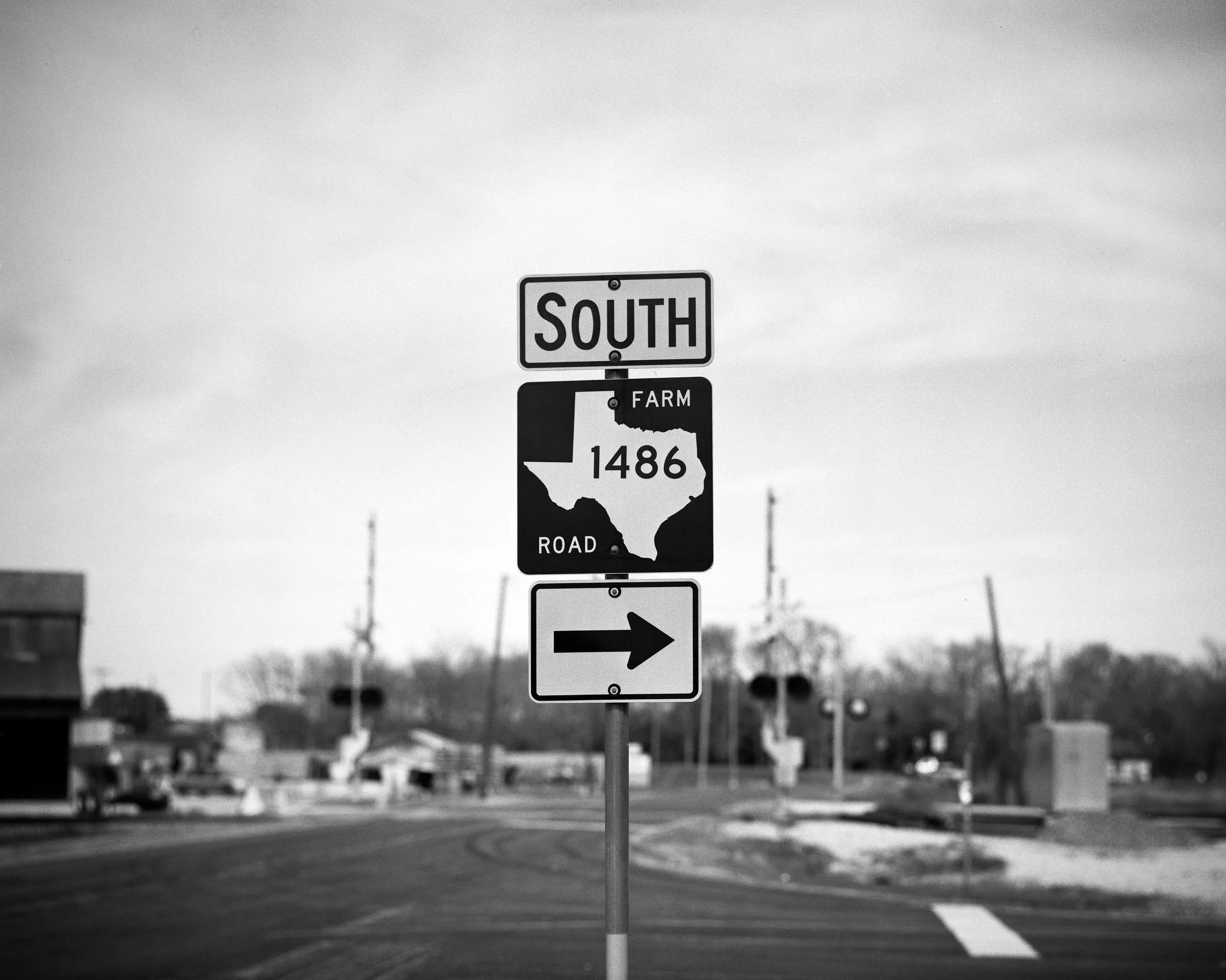 Black and white photo of a road sign indicating southbound direction on Road 1486, with an arrow pointing to the right, in a semi-rural area.