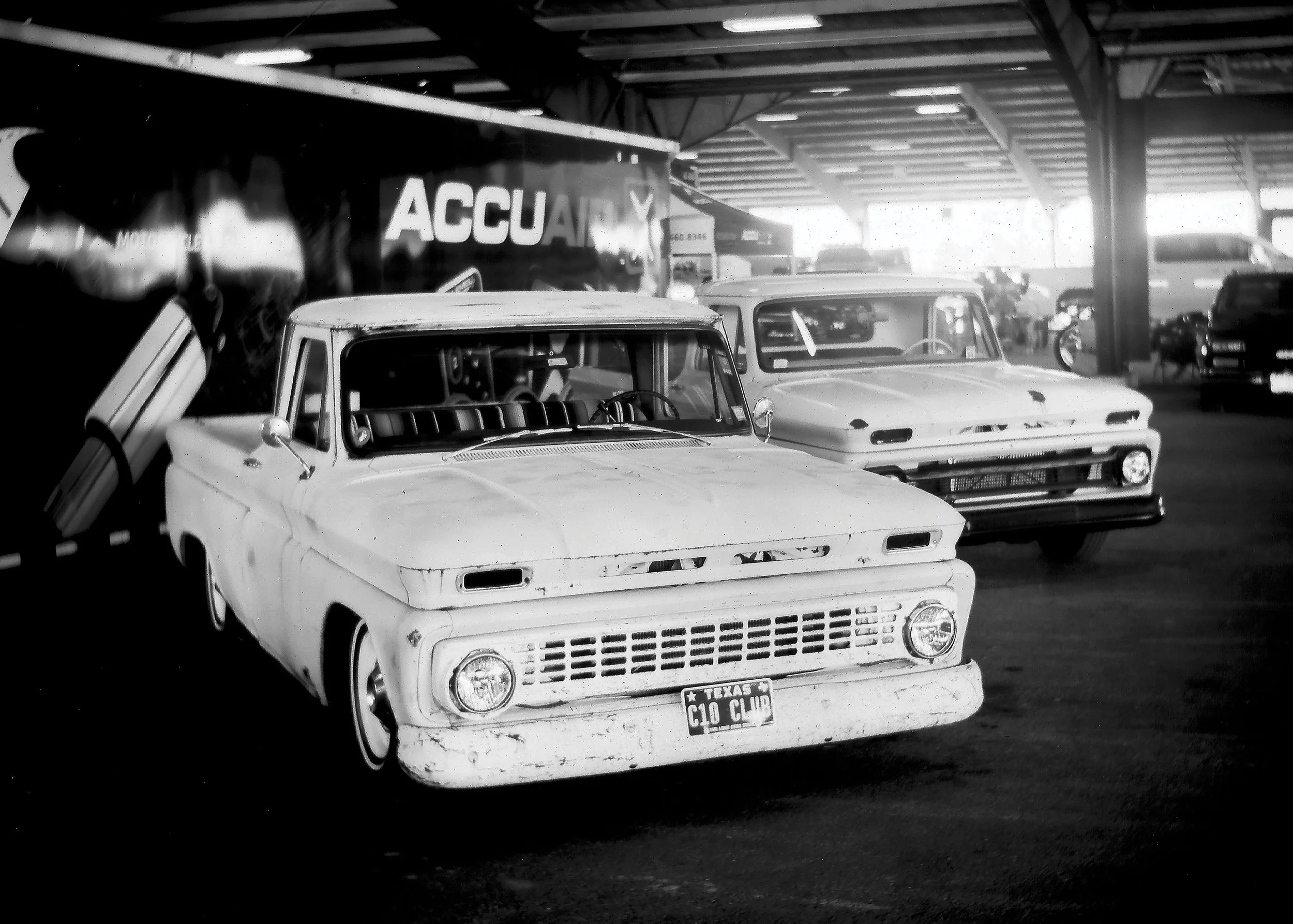 Black and white photo of vintage cars parked in an indoor garage with a large advertisement banner in the background.