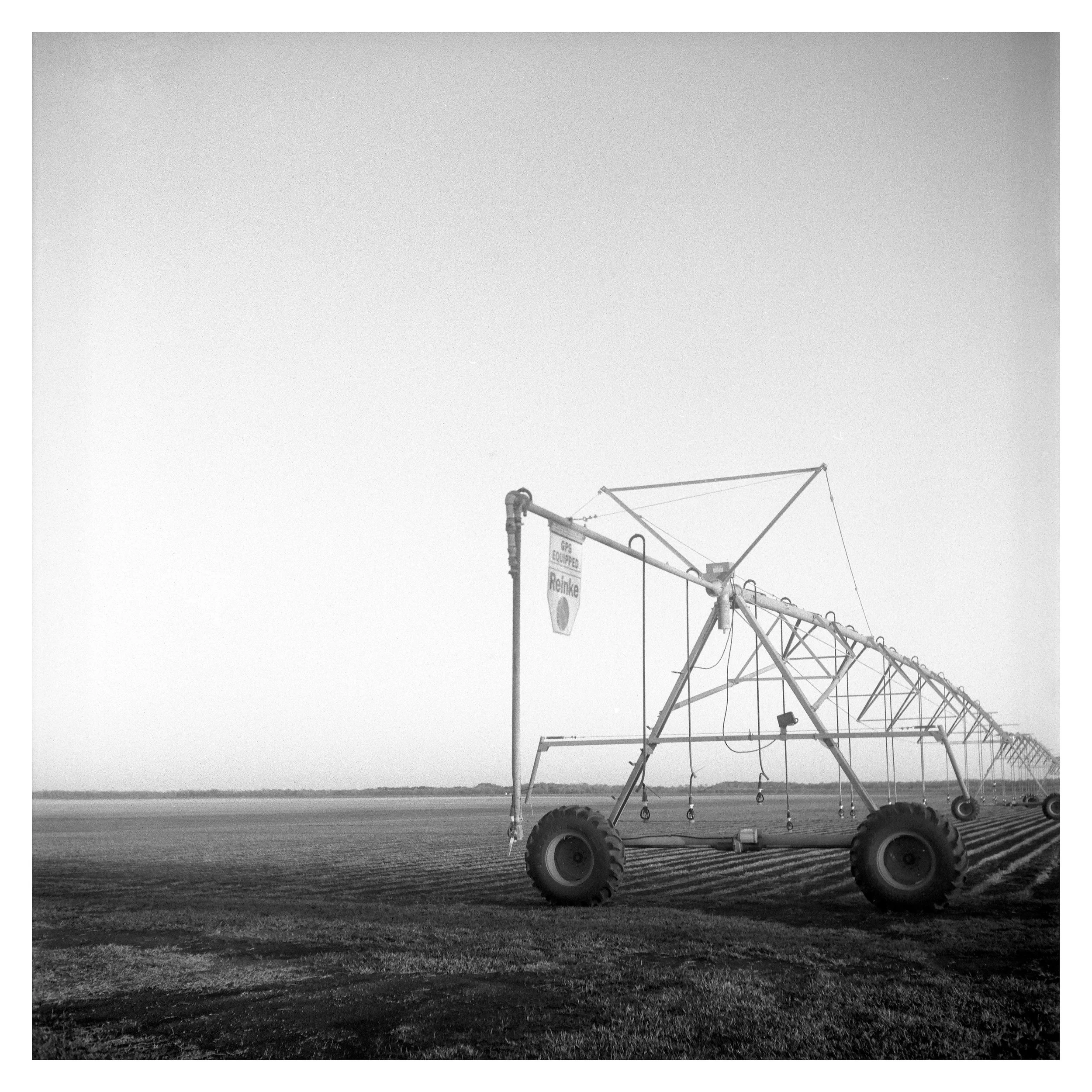 A large agricultural irrigation sprinkler system with wheels, set in a wide open field, in black and white.