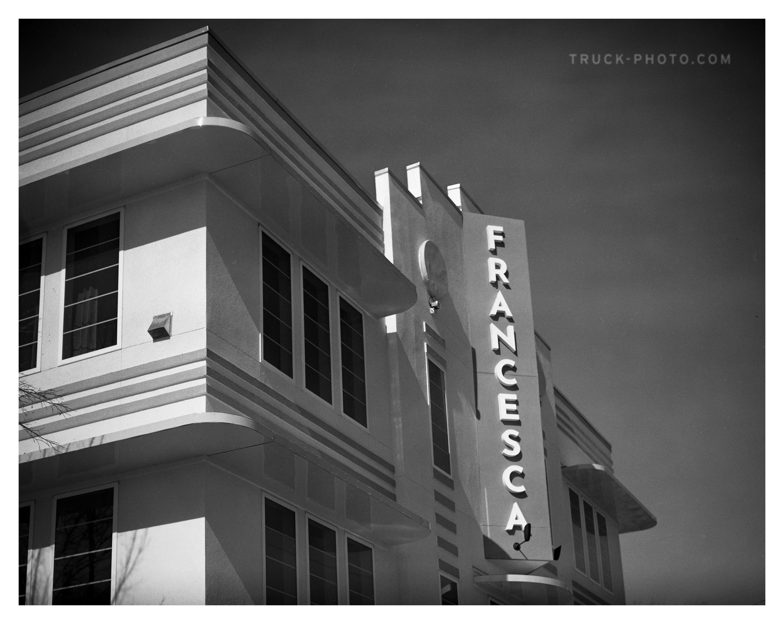 Black and white photograph of a mid-century modern building with a vertical sign that reads "FRANCESCA" attached to the front facade.