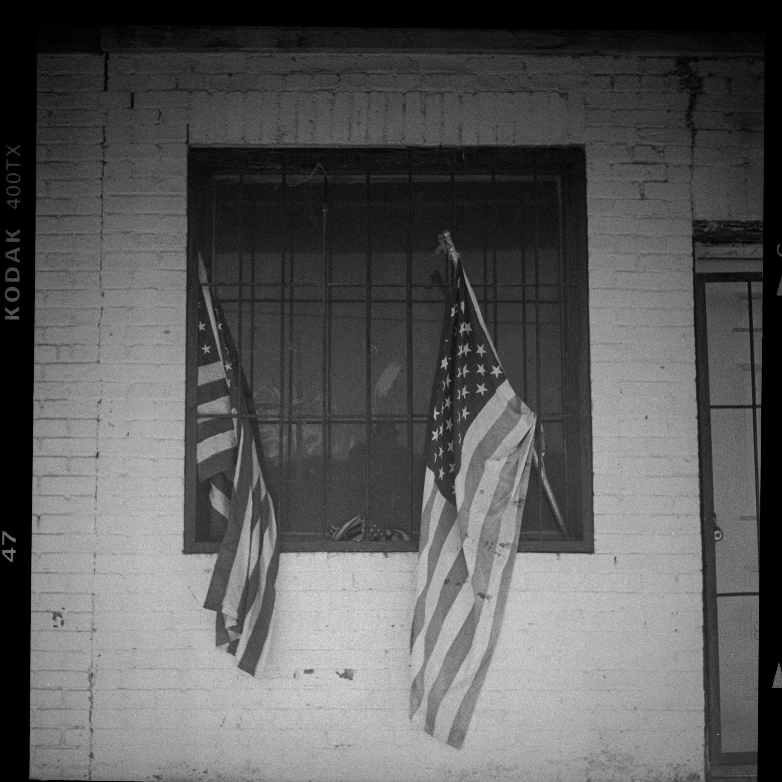 Two American flags hanging outside a window with metal bars in a brick building.