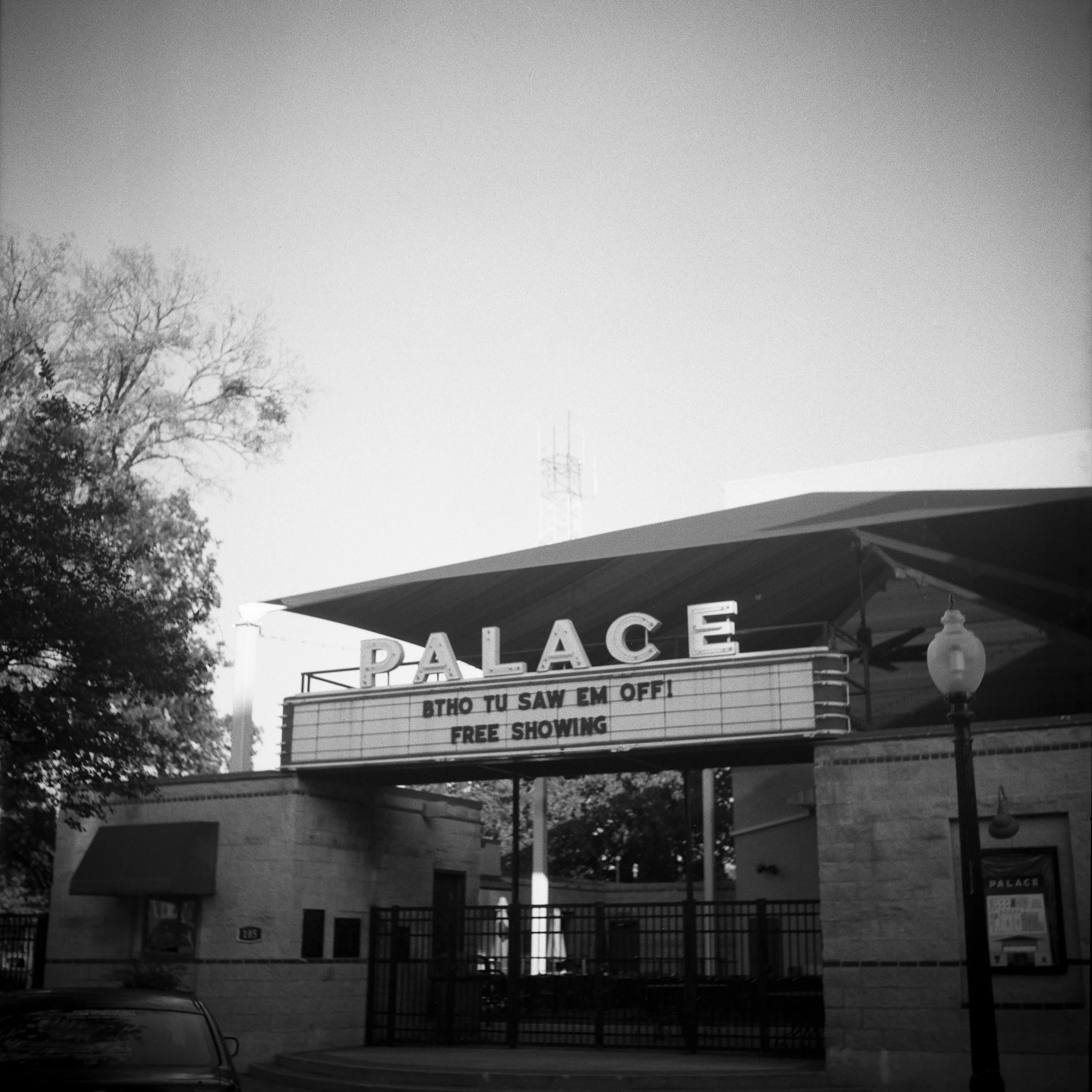 Black and white photo of a movie theater with a marquee that reads 'PALACE' and additional text 'BTHO TU SAW EM OFF! FREE SHOWING'.