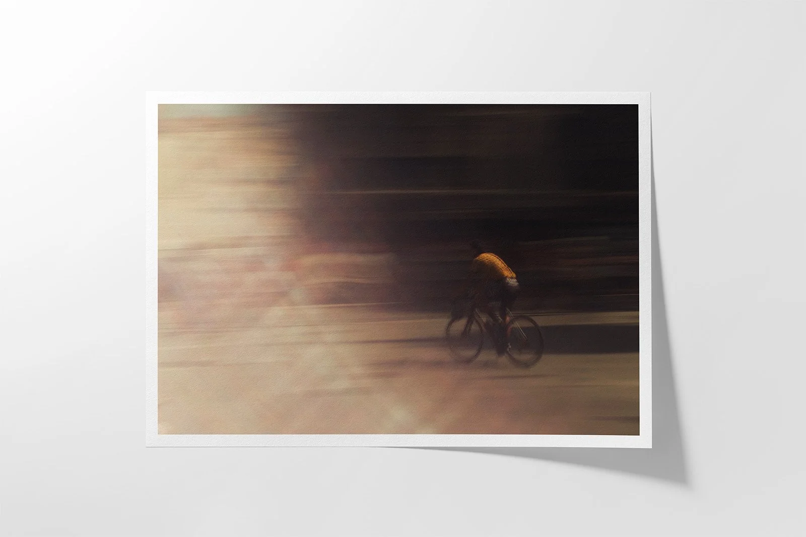 A person riding a bicycle with motion blur effects, wearing a bright orange helmet and dark clothing, against a dark background.