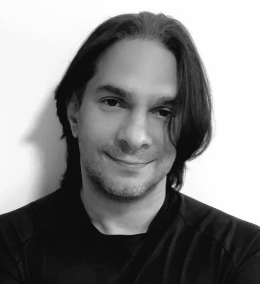 Black and white photo of a man with shoulder-length dark hair, smiling and wearing a dark shirt.