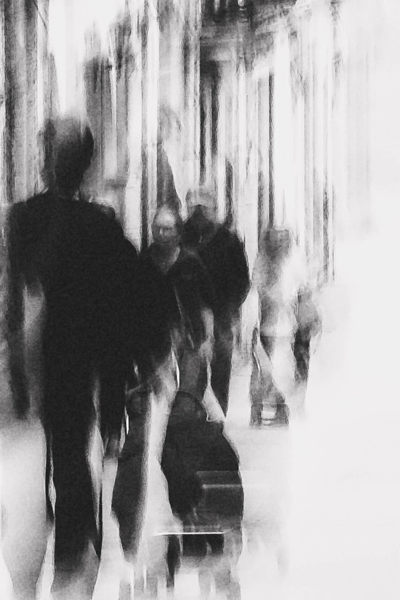 People walking through an airport terminal, some pulling luggage, in a blurred black-and-white image.