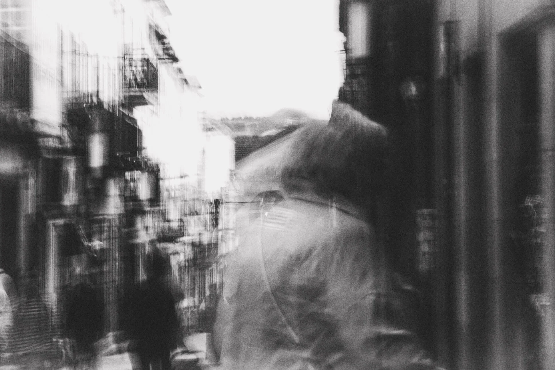 Double exposure black and white photograph of a city street with buildings and people, creating a layered effect.