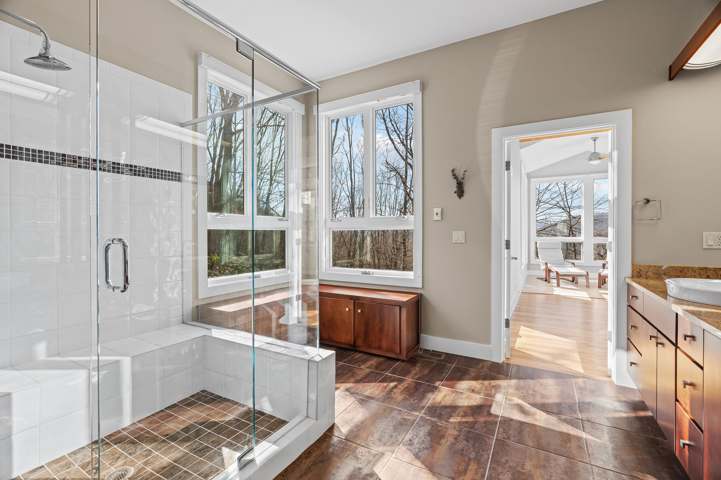 Bathroom with walk-in shower, large windows, wooden bench, and doorway to an adjacent room with seating