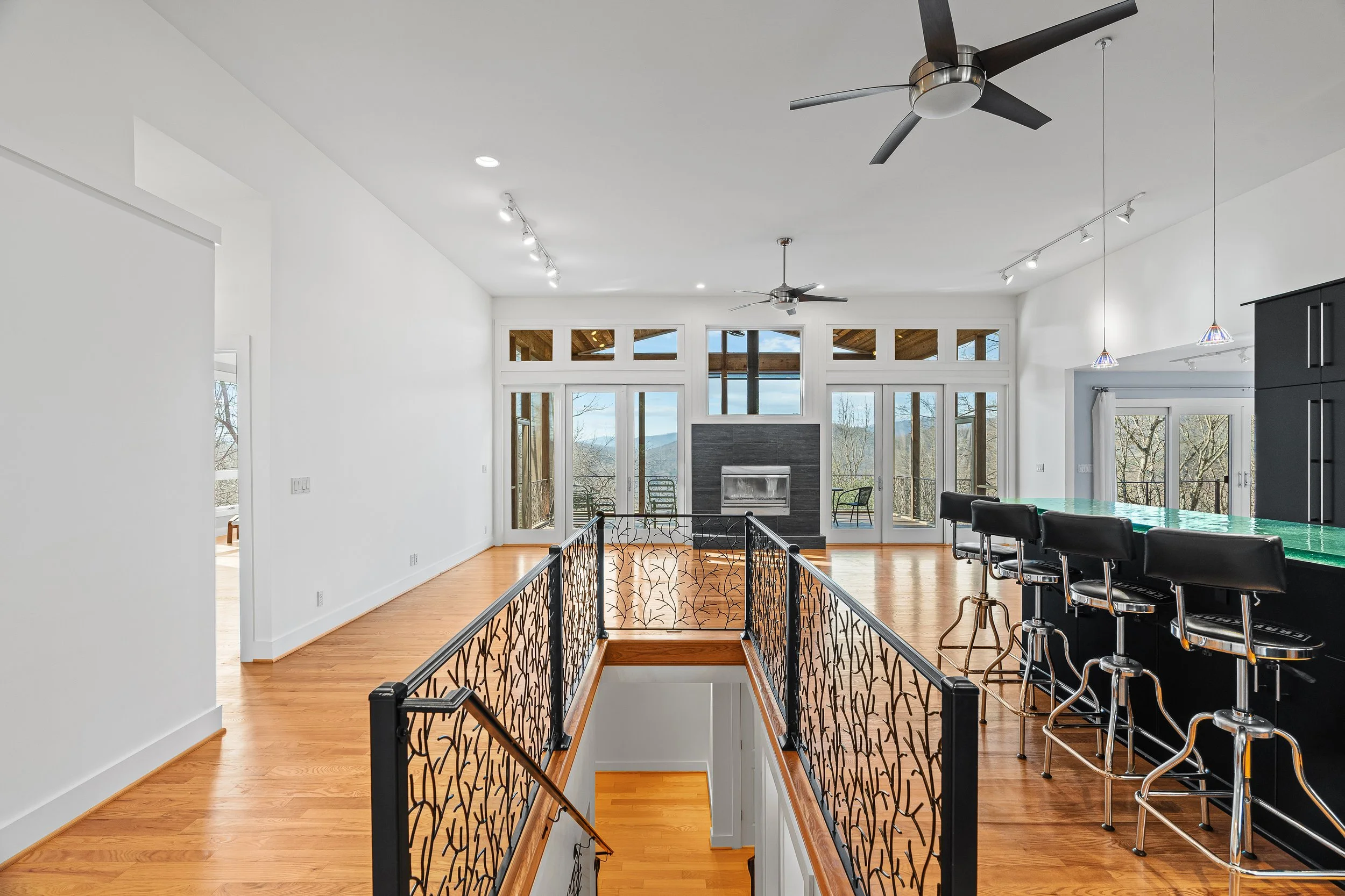 Open-concept living area with hardwood floors, a fireplace, large windows with mountain views, and a bar counter with black chairs.