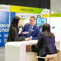 People interacting at a trade show booth with General Electric signage.