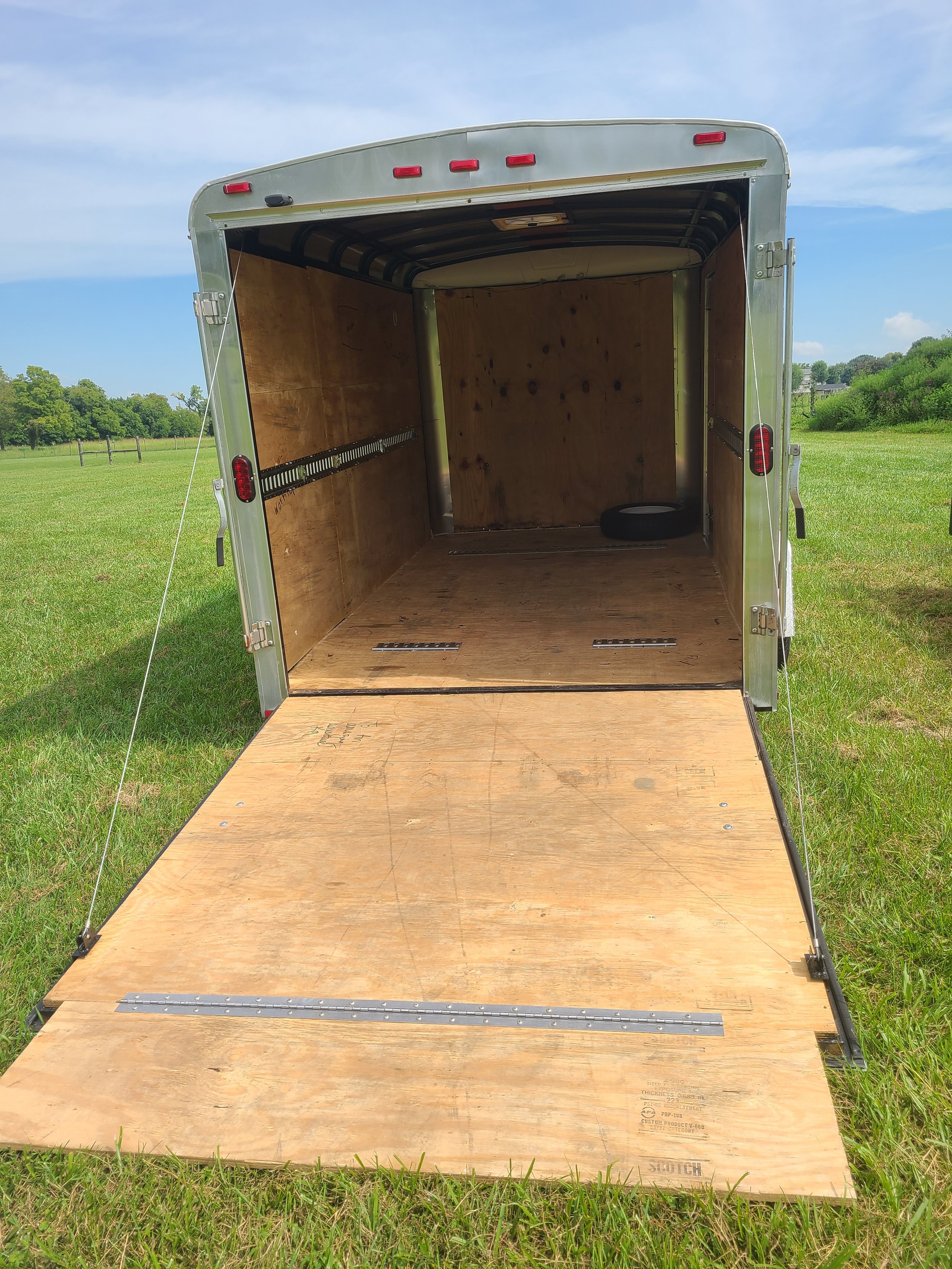 Open utility trailer with wooden interior and ramp on grassy field