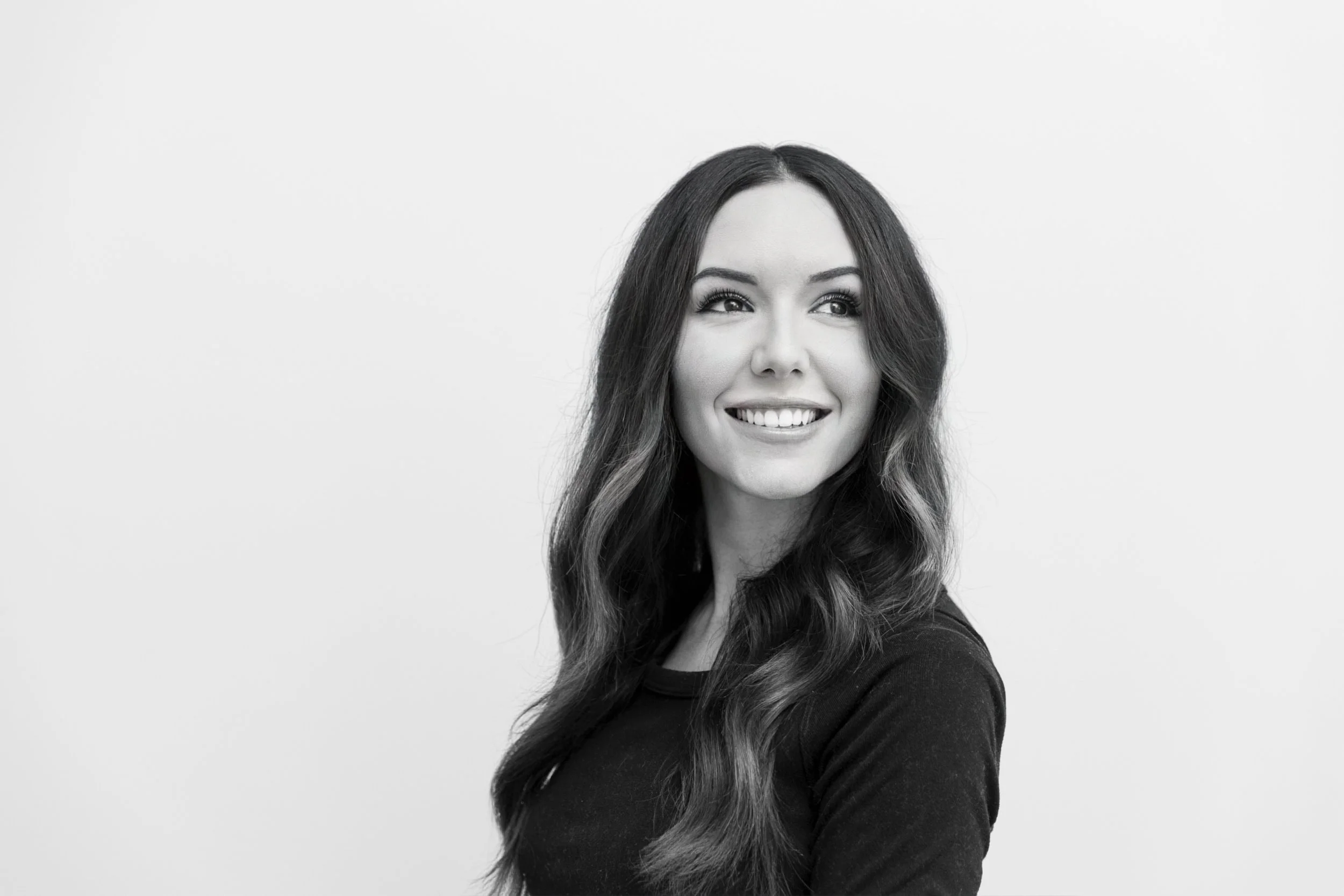 Black-and-white portrait of a smiling woman with long wavy hair, looking to her left, against a plain light background.